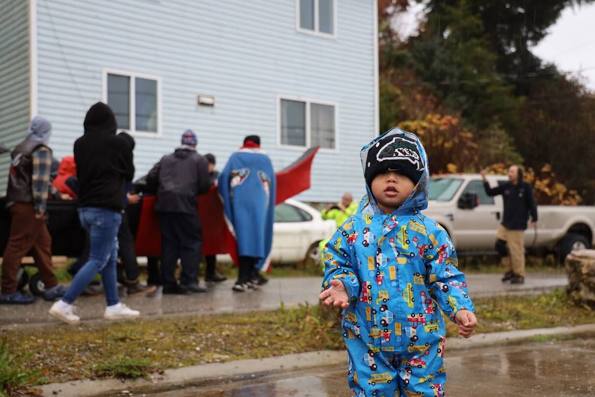 Rooney Hasselquist, 1, stands on the sidewalk of Front Street as residents of Angoon push the first dugout canoe made in Angoon since the U.S. Navy bombardment exactly 140 years ago. Hasselquist walked down to watch the event with the help of his mother Katherine Nelson. (Clarise Larson / Juneau Empire)