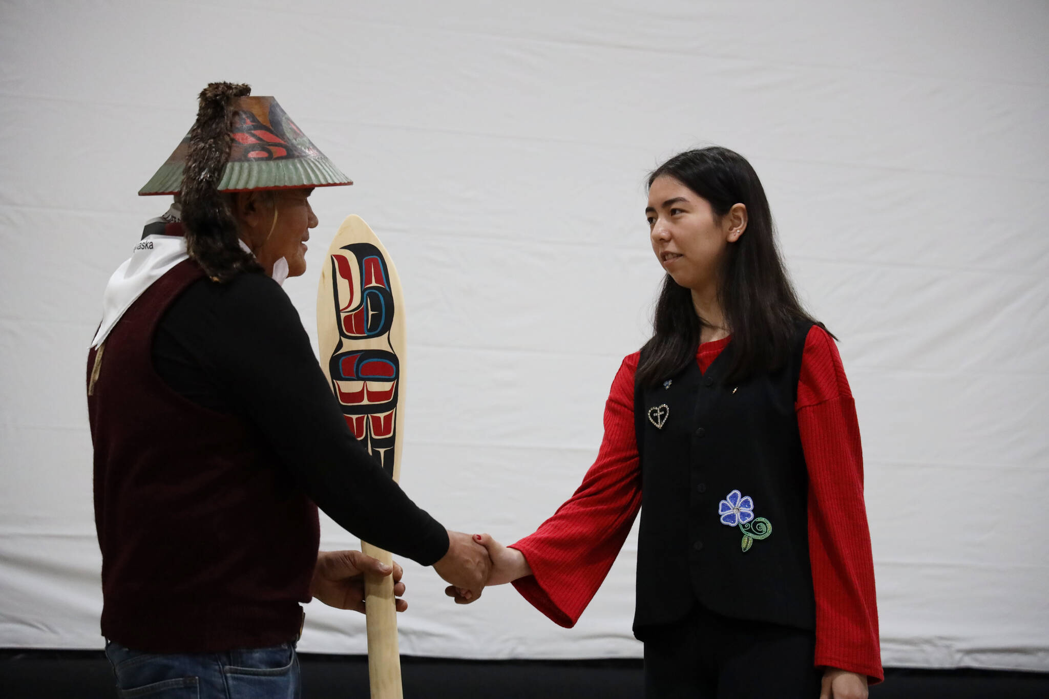Tlingit master carver Wayne Price shakes hands with a student from Chatham School District after being gifted a painted wooden paddle made by the students. (Clarise Larson / Juneau Empire)