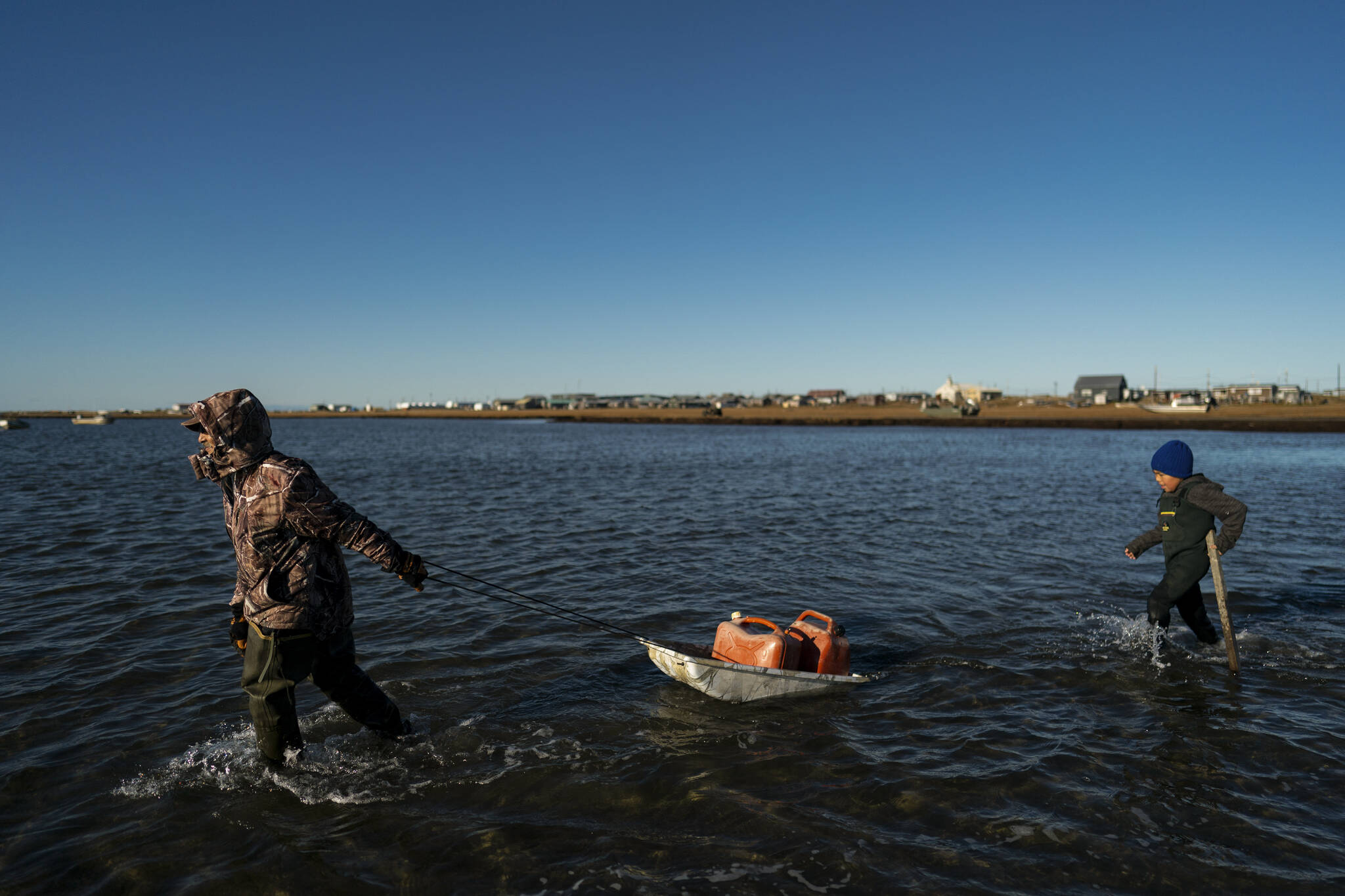 AP Photo / Jae C. Hong 
Pulling a sled with fuel containers in the lagoon, Joe Eningowuk, 62, left, and his 7-year-old grandson, Isaiah Kakoona, head toward their boat through the shallow water while getting ready for a two-day camping trip in Shishmaref, Alaska, Saturday, Oct. 1, 2022. Rising sea levels, flooding, increased erosion and loss of protective sea ice and land have led residents of this island community to vote twice to relocate. But more than six years after the last vote, Shishmaref remains in the same place because the relocation is too costly.
