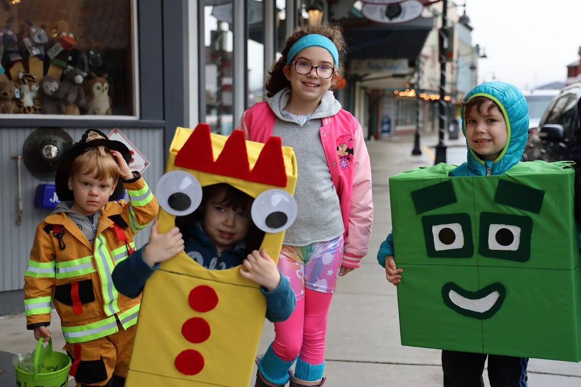 Luke, Wesley and Elsie Stevens smile alongside  other trick-or-treaters as they walk down Franklin Street Monday afternoon during the downtown trick-or-treat event. (Clarise Larson / Juneau Empire)