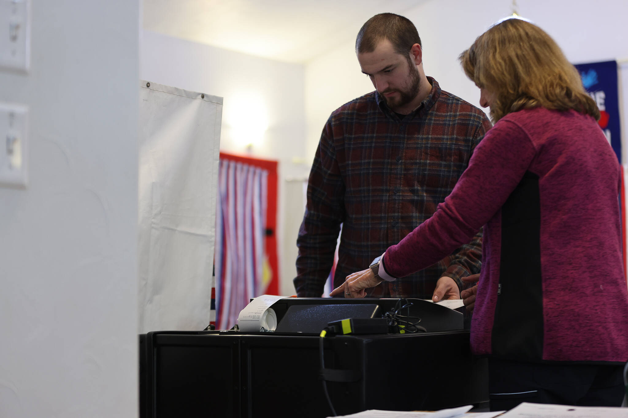 Michael Blackwell watches the screen on the voting machine while poll worker Peggy Cowarn gestures toward the portion whether the ballot has been accepted. (Ben Hohesntatt / Juneau Empire)