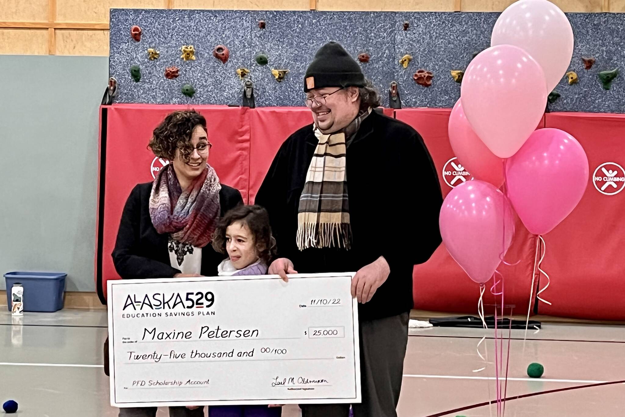 Maxine Petersen, 8, stands with her parents Carl Petersen and Samantha Jenkins to accept the Alaska 529 annual $25K Giveaway at Kax̱dig̱oowu Héen Elementary