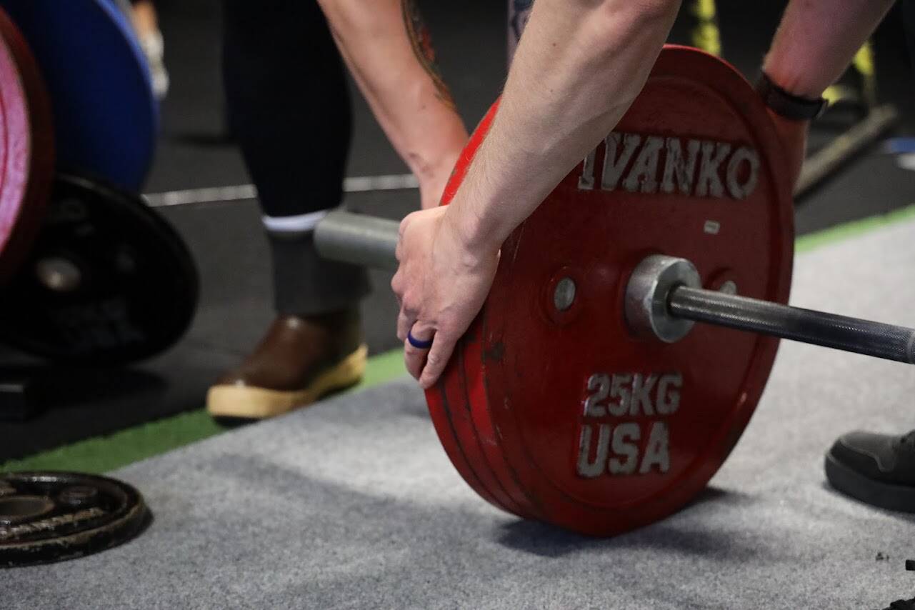 Volunteers add weight to the bar Saturday afternoon at Juneau’s Tongass Fitness for a powerlifting competition. (Clarise Larson / Juneau Empire)