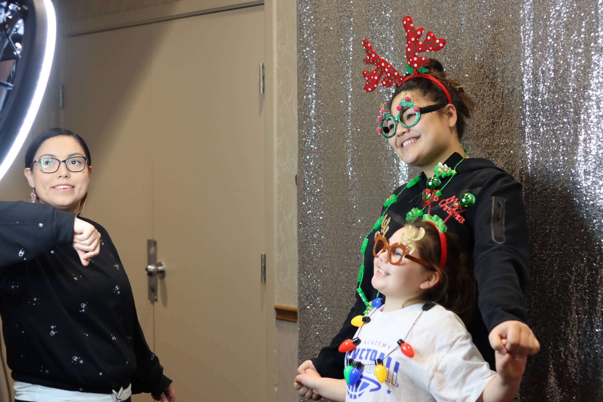 Tlingit and Haida volunteer Vanessa Allen helps young Dylann Wilson and Penina Fenumiai with the holiday photo booth set up during the Indigenous Artists & Vendors Holiday Market at the Elizabeth Peratrovich Hall on Friday. (Jonson Kuhn / Juneau Empire)
