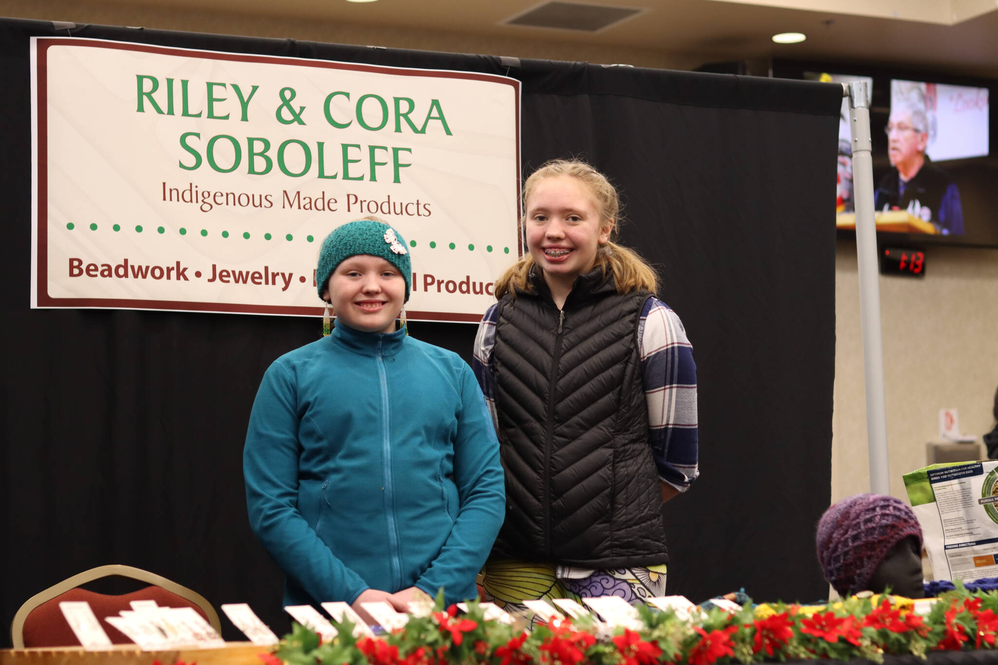 Sisters Riley and Cora Soboleff stand with their art booth which was featured for the first time at the Indigenous Artists & Vendors Holiday Market on Friday. The Dzantik’i Heeni Middle Schoolers make their own winter hats and assorted earrings. (Jonson Kuhn / Juneau Empire)