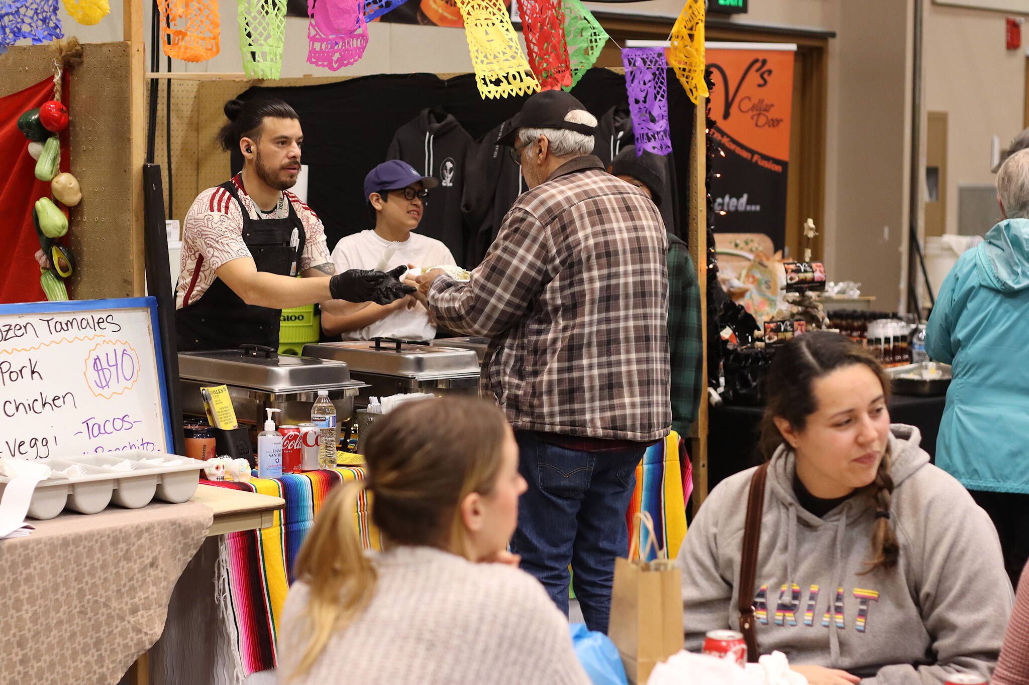 A food vendor sells tamales to a customer Saturday at the Juneau Public Market. Locally-made hot foods as well as gifts such as baked goods are being sold by vendors through the three buildings where market events are taking place. (Mark Sabbatini / Juneau Empire)