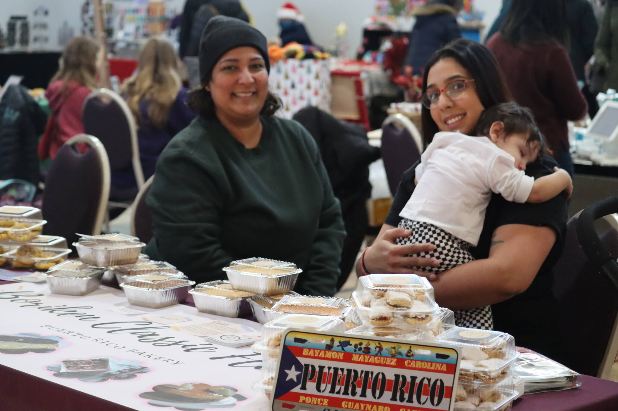 Neyshmy Sandoval and her mother Malena and baby Luna sell Puerto Rican homemade desserts with Boriken Classic Flavor at Juneau Arts and Humanities Council’s annual Stocking Stuffer Showcase on Saturday the Juneau Arts and Culture Center. (Jonson Kuhn / Juneau Empire)