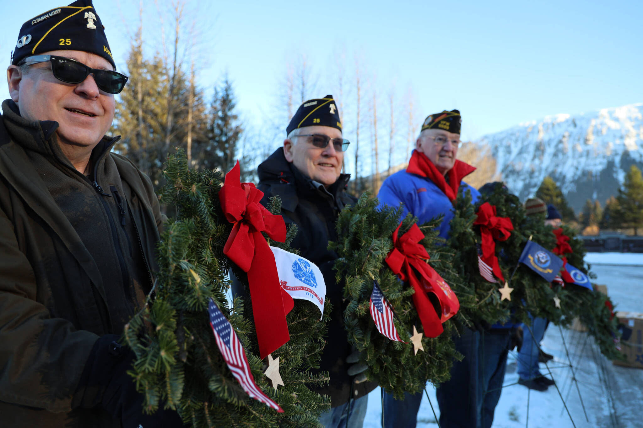 From left to right, Duff Mitchell, Army National Guard veteran, Bill Clutton, Army veteran, and Tom Dawson, Navy veteran stand in a line holding wreaths during a laying of wreaths ceremony for National Wreaths Across America Day on Saturday afternoon. (Clarise Larson / Juneau Empire)