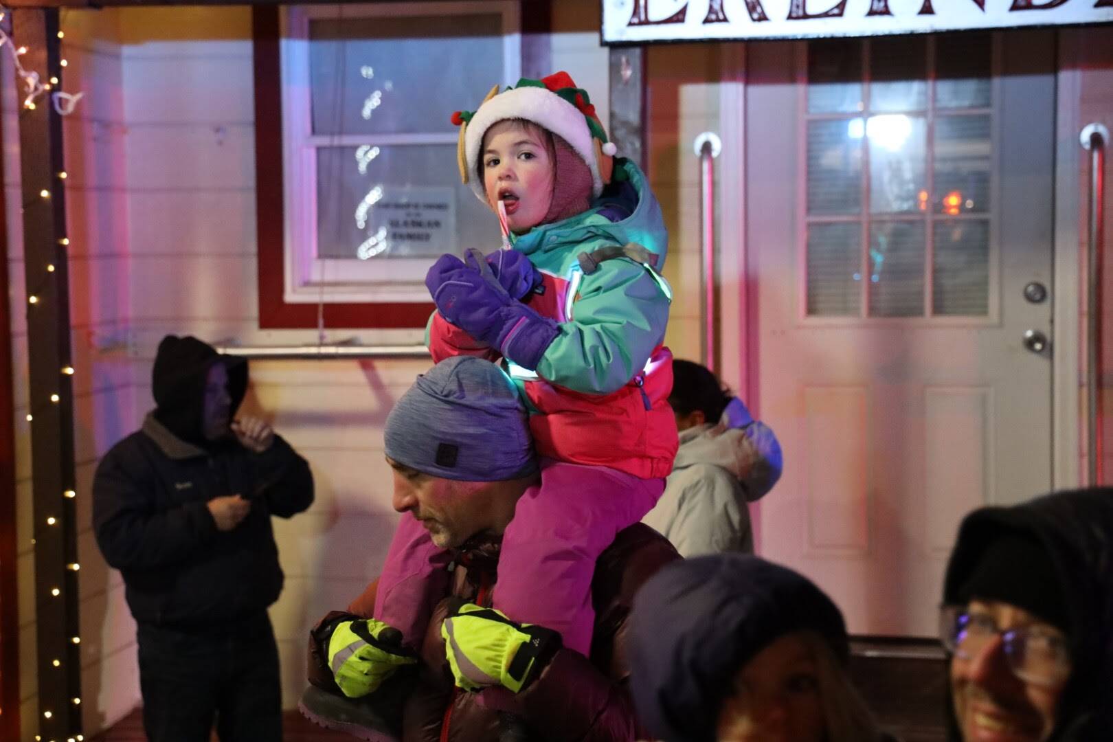 Liesel Thier, 4, snacks on a candy cane while on the shoulders of her dad during the downtown Santa parade Saturday evening. (Clarise Larson / Juneau Empire)