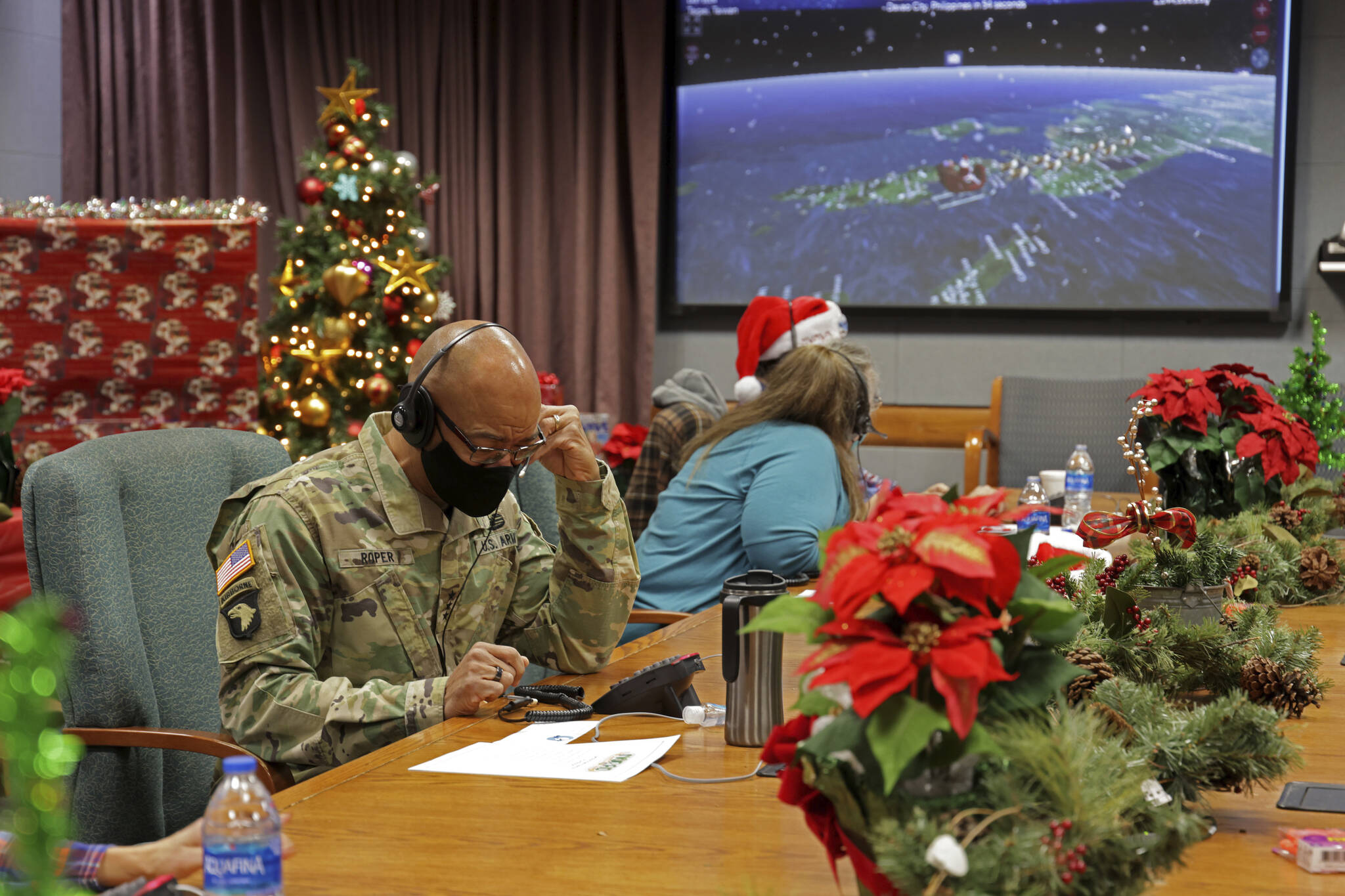 In this photo released by the U.S. Department of Defense, volunteers answer phones and emails from children around the globe during annual NORAD Tracks Santa event at Peterson Air Force Base in Colorado Springs, Colo., on Dec. 24, 2021. The U.S. military agency known for tracking Santa Claus as he delivers presents on Christmas Eve doesn’t expect COVID-19 or the “bomb cyclone” hitting North America to impact Saint Nick’s global travels this year. NORAD, the North American Aerospace Defense Command, is responsible for monitoring and defending the skies above North America. (Jhomil Bansil / U.S. Department of Defense)