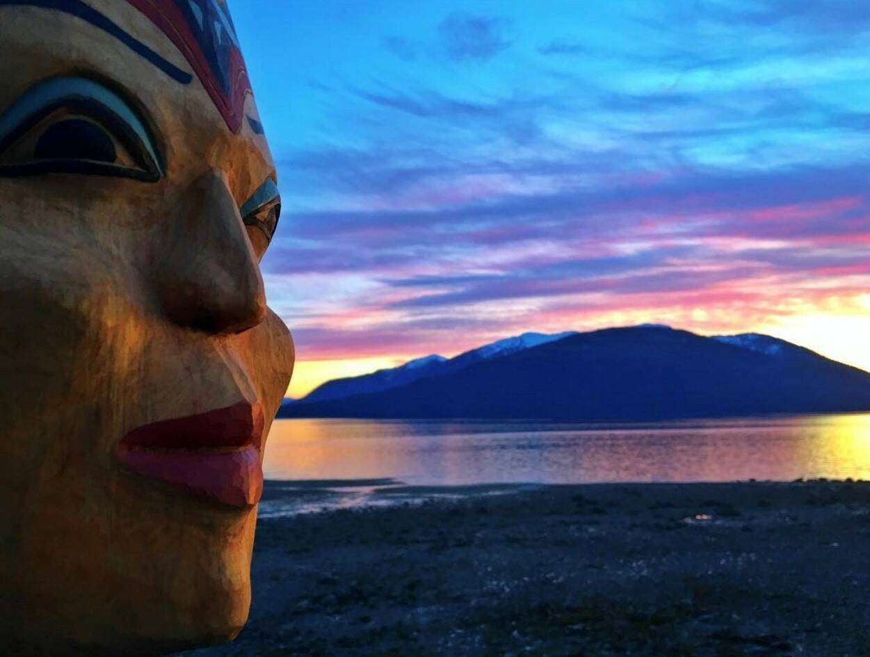Raven Woman mask by Kristina Cranston is seen in front of a vibrant Wrangell sunset. (Vivian Faith Prescott / For the Capital City Weekly)