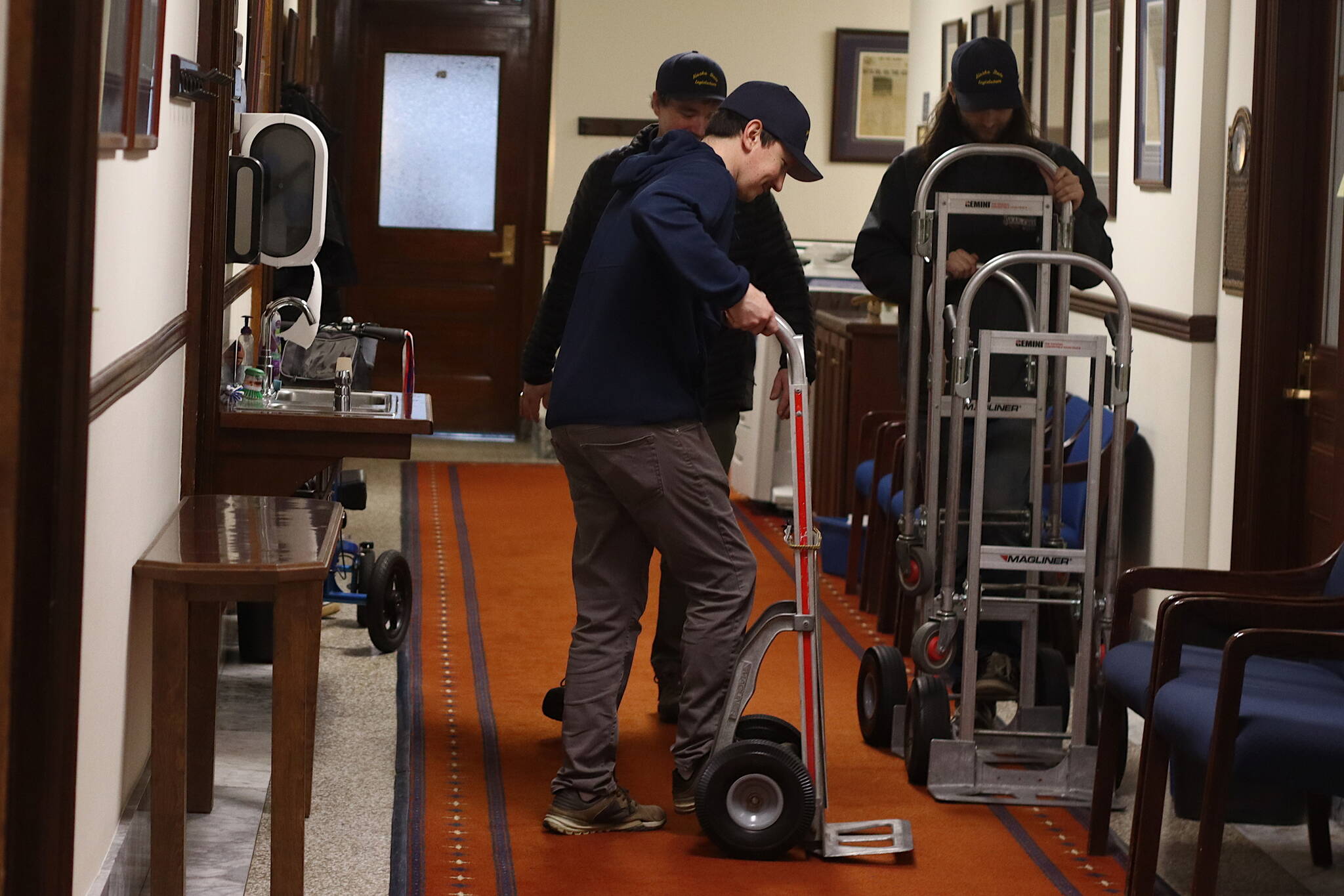 Logistics employees push hand trucks down a hallway at the Alaska State Capitol on Friday after placing chairs in the Senate chamber. (Mark Sabbatini / Juneau Empire)