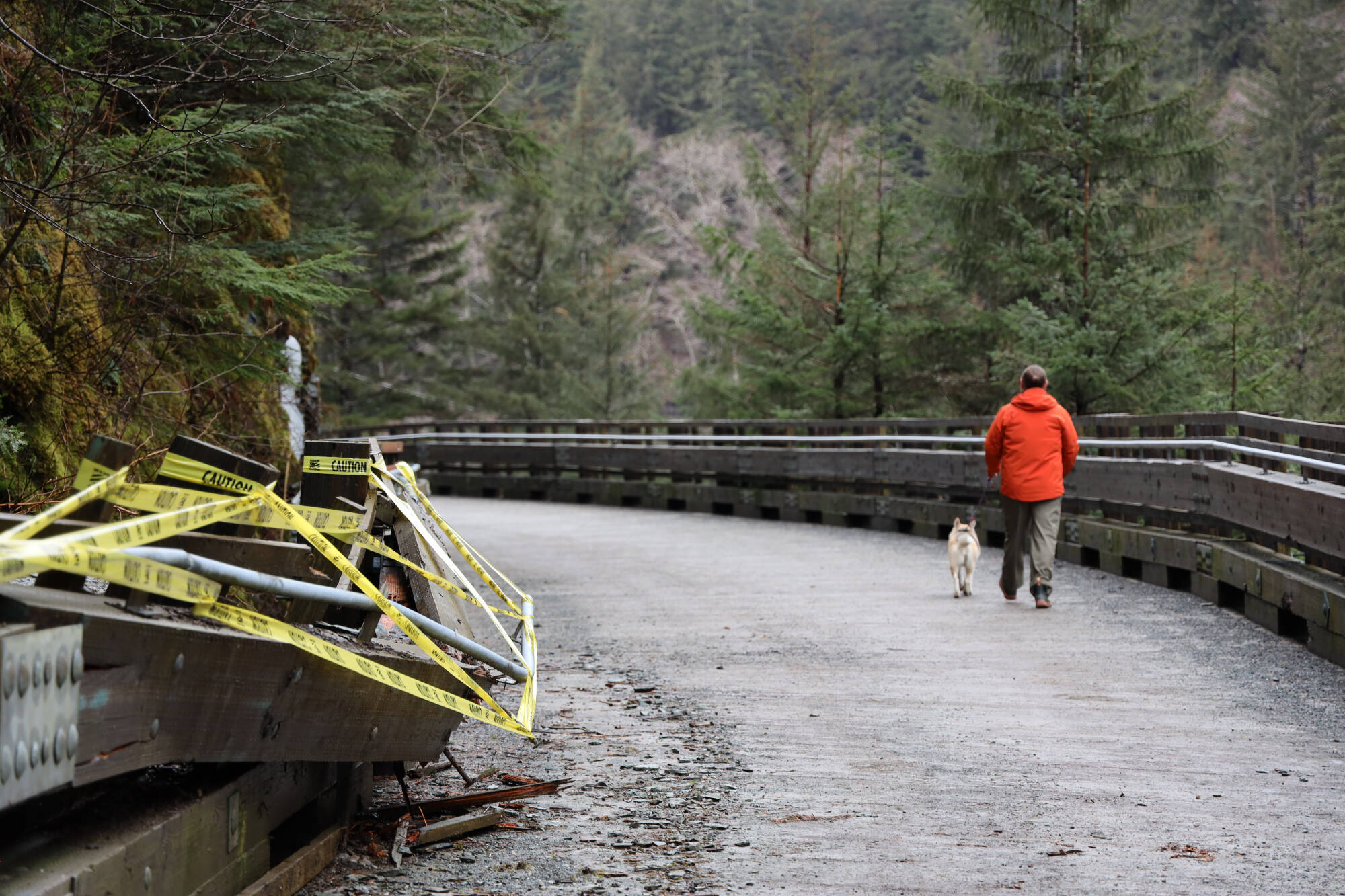 A resident and his dog walk past the taped off portion of the Basin Road Trestle after it suffered damaged from a rockslide earlier this week. The trestle is open to pedestrians, but will remain closed to vehicular traffic until structural repairs are made, according to city officials. (Clarise Larson / Juneau Empire)
