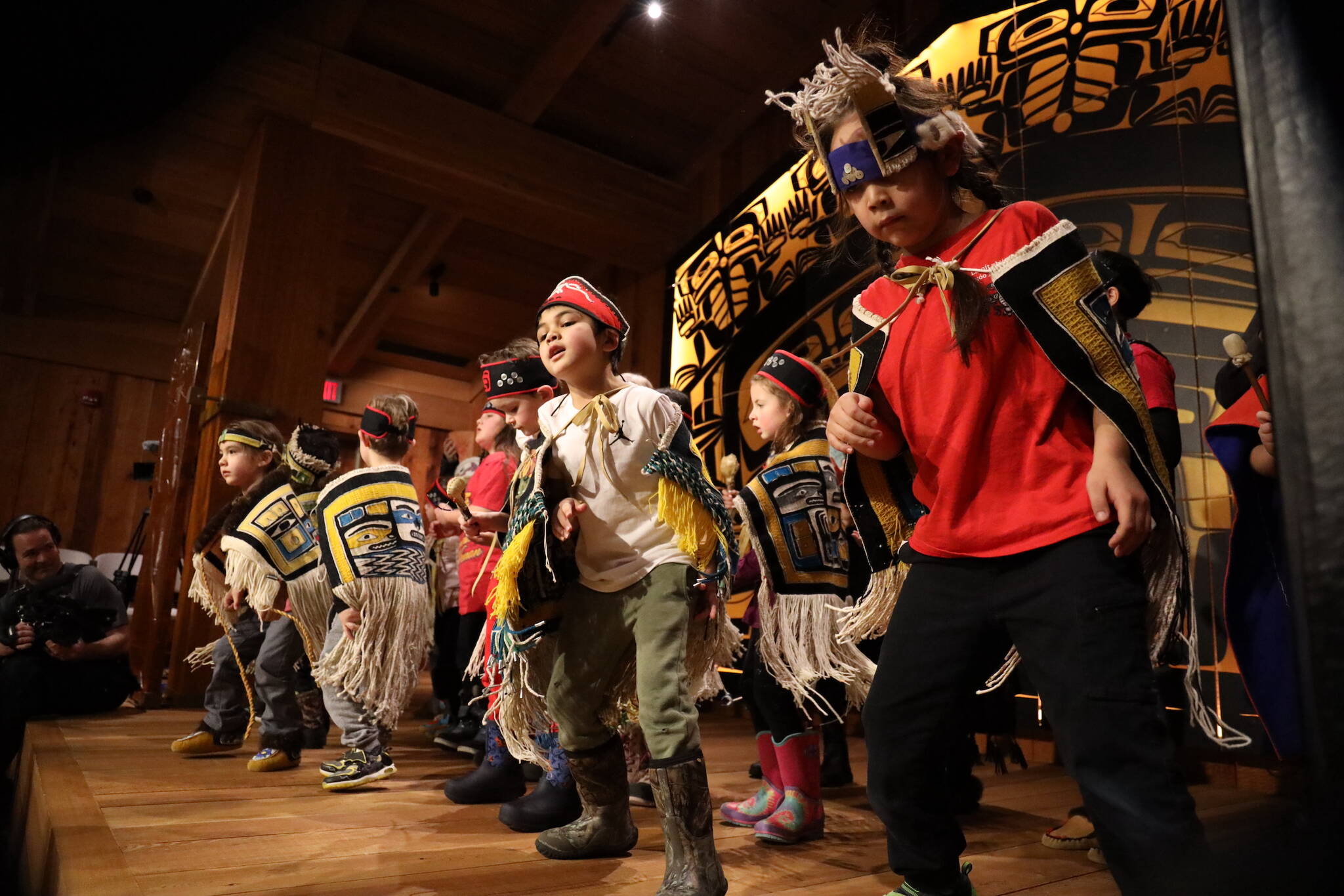 Young students from the Tlingit Culture Language and Literacy program at Harborview Elementary School dance on stage Wednesday afternoon during a dancing-of-the-robes ceremony for over a dozen Chilkat robes that were weaved by student weavers who participated in a more than two-year-long apprenticeship to learn the craft. (Clarise Larson / Juneau Empire)