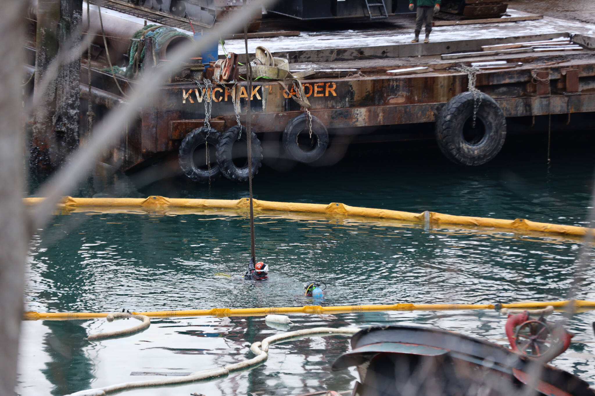 Divers manuever in the water to prepare slings to be placed surrounding a a privately owned 107-foot tugboat that is being recovered by the Coast Guard after it sunk in late December. (Clarise Larson / Juneau Empire)