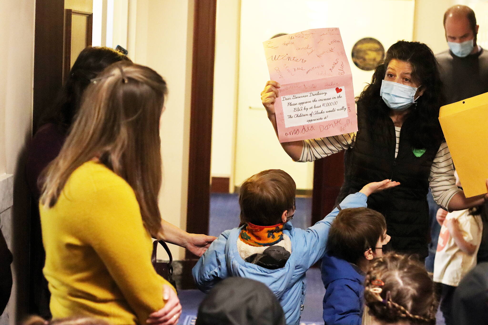 Lupita Alvarez, a teacher at the Montessori Borealis preschool program, offers a Valentine’s Day card signed by youths in the Juneau program to a member of Gov. Mike Dunleavy’s legislative staff outside his office on the third floor of the Alaska State Capitol on Monday. The students were lobbying for an increase in education funding, which the governor is proposing remain flat in his budget for next year. (Mark Sabbatini / Juneau Empire)