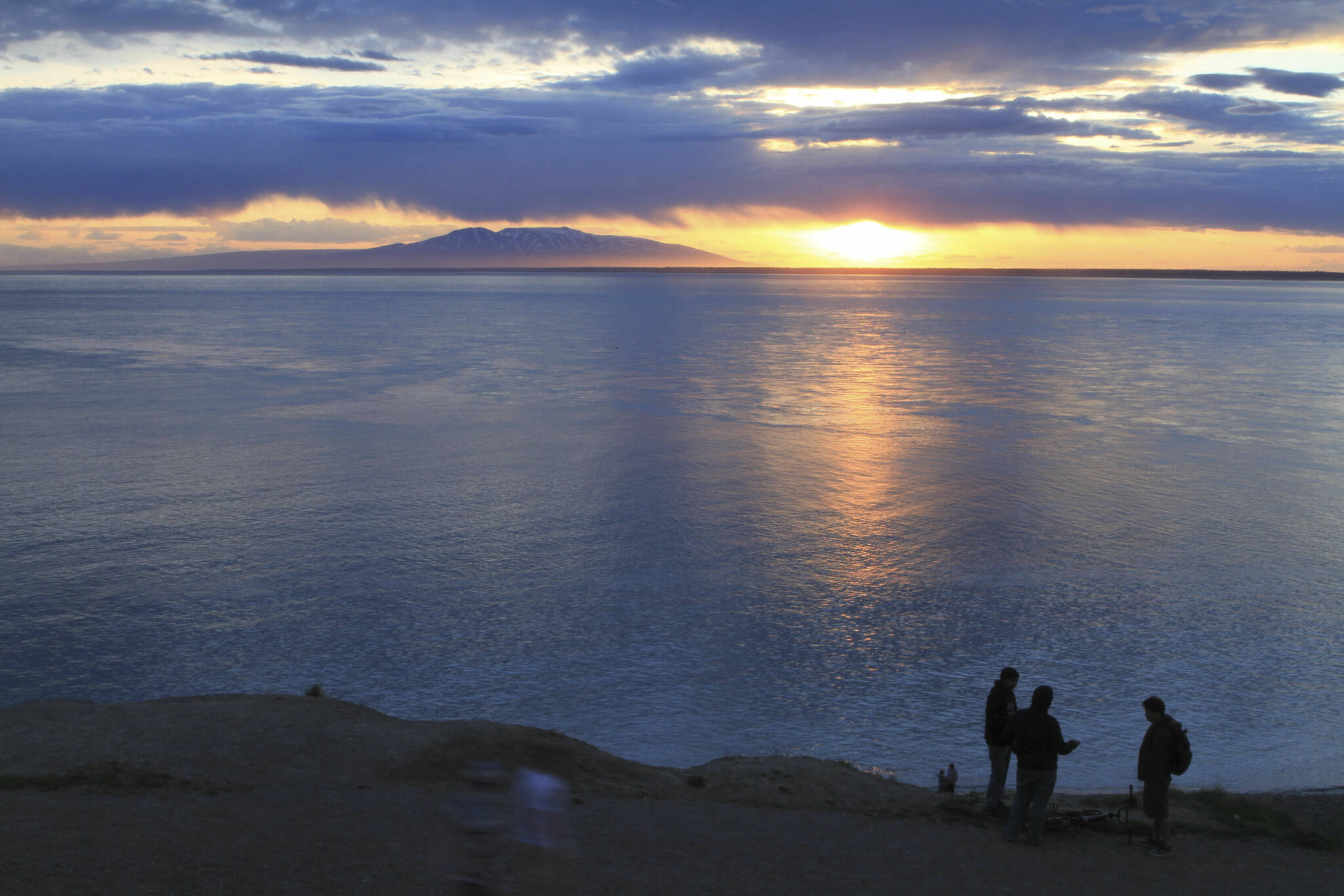 Visitors to Point Woronzof Park watch the sun set over Cook Inlet and Mount Susitna, also known as Sleeping Lady, on June 7, 2013, in Anchorage, Alaska. Alaska Gov. Mike Dunleavy has proposed a plan that could use the Cook Inlet basin for carbon sequestration. (AP Photo / Dan Joling)