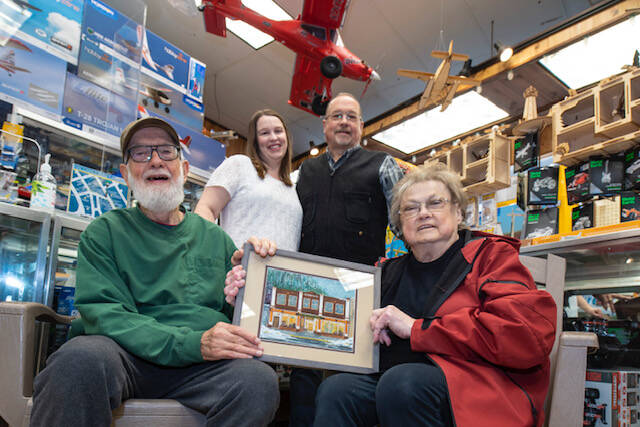 The three generations of Wileys who have operated the Ben Franklin Store are shown inside the shop. Seated are Fred and Sally Wiley, holding a painting of the 1930s Blomgren Building. Standing are Meagan Wiley Bishop and her father Mike Wiley who currently run the popular downtown Front Street business. (Michael Penn / Downtown Business Association)