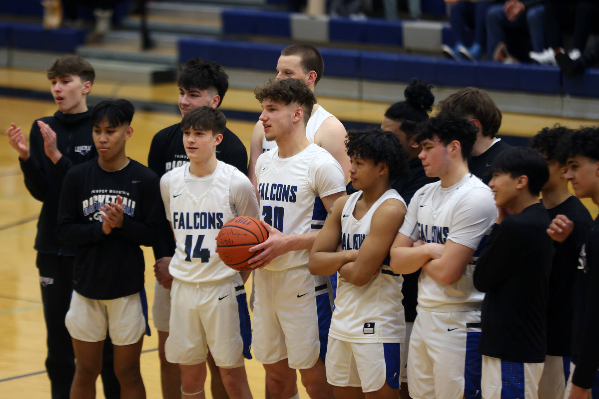 TMHS junior Thomas Baxter (center, holding a ball) stands with teammates before a 64-59 home win against Ketchikan as he is recognized for breaking the 1,000-point mark. (Ben Hohenstatt / Juneau Empire)