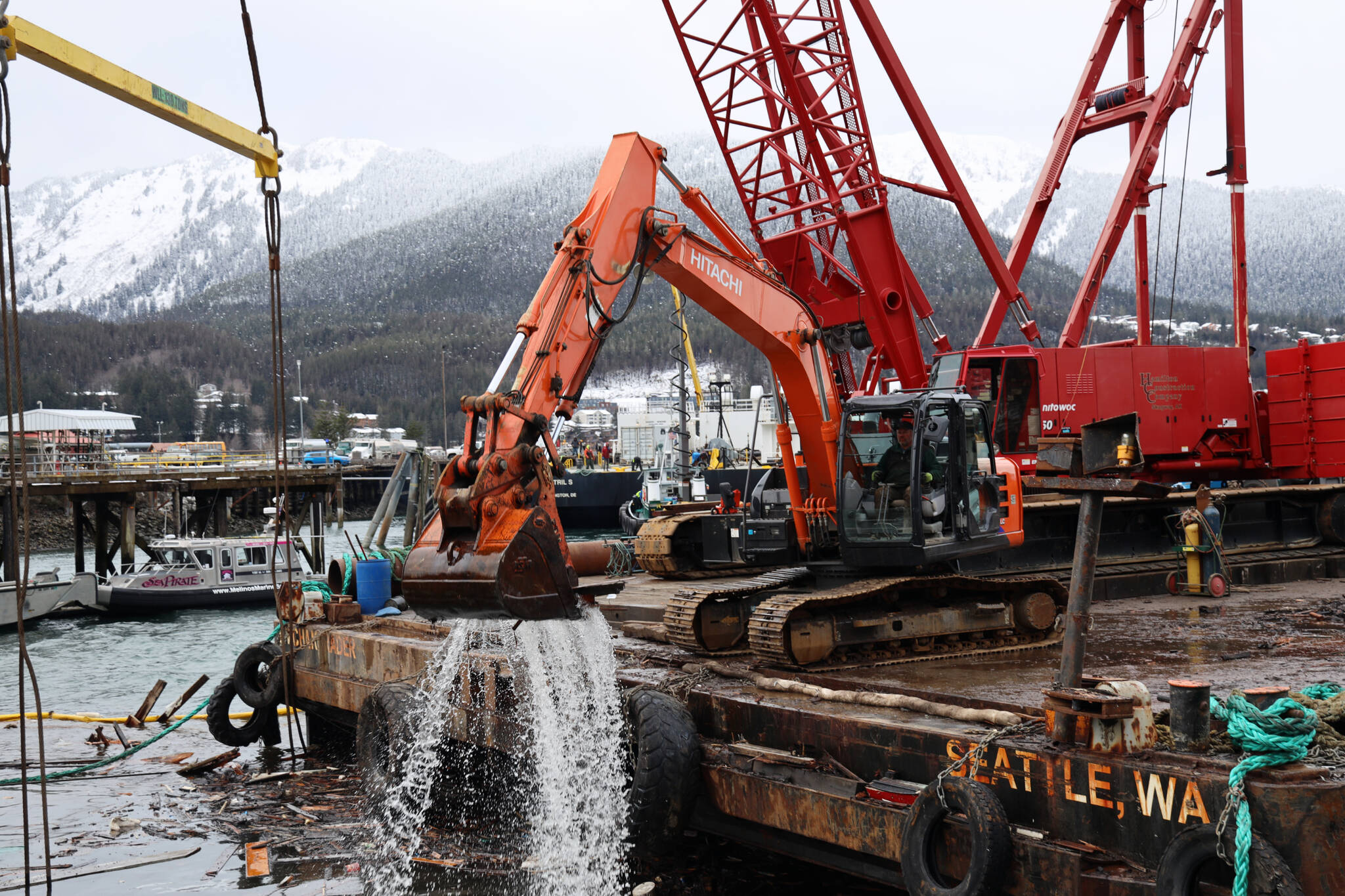 An excavator on a barge scoops floating debris near the shore of Gastineau Channel on Monday morning. The effort was a part of the recovery process of a 107-foot tugboat that sank at a dock south of the cruise ship docks in late December. (Clarise Larson / Juneau Empire)