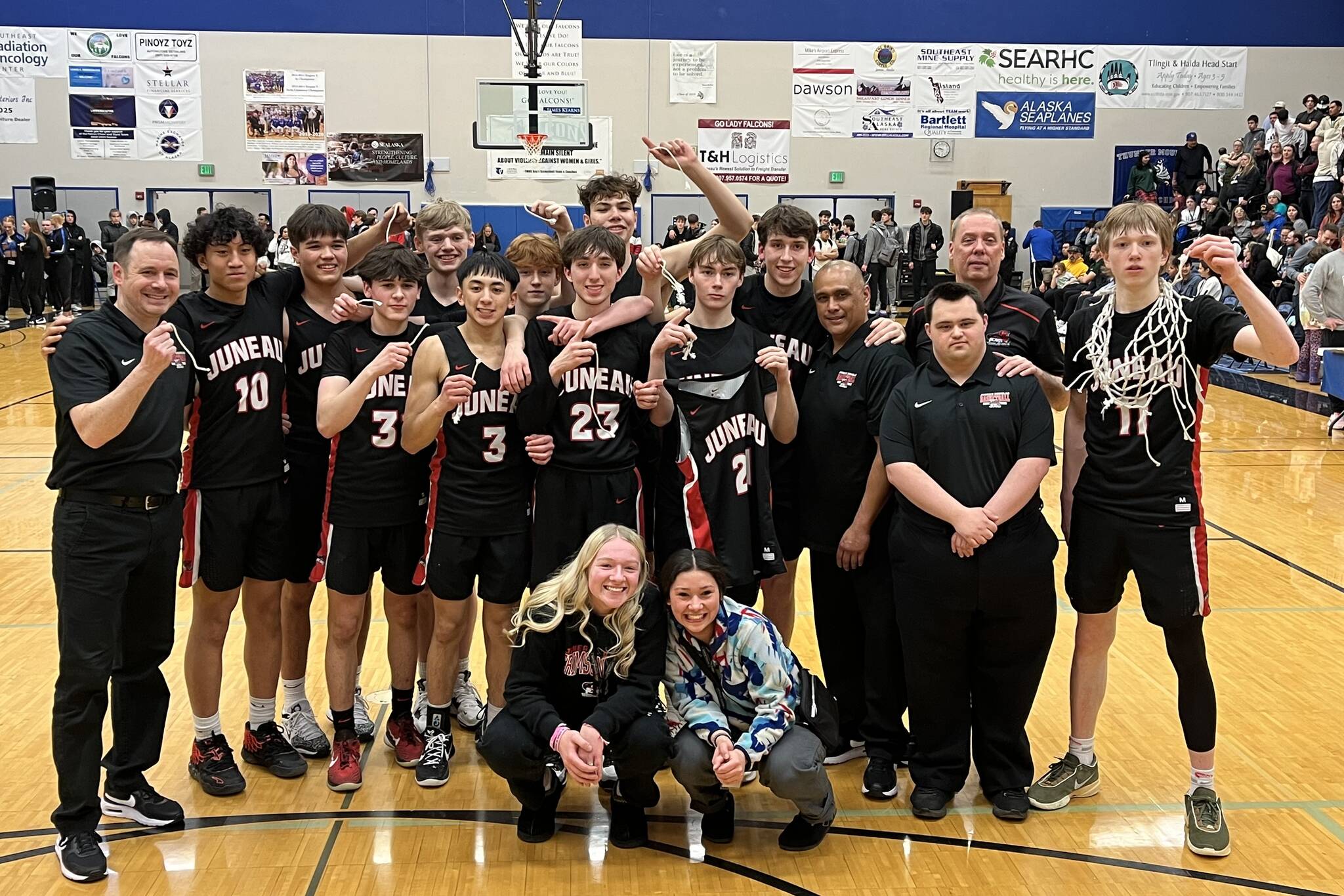 The JDHS Crimson Bears basketball team poses for a victory photo after the net cutting ceremony on Saturday. The Bears beat Ketchikan High School in a second tournament game, securing the team’s spot at state. (Jonson Kuhn / Juneau Empire)