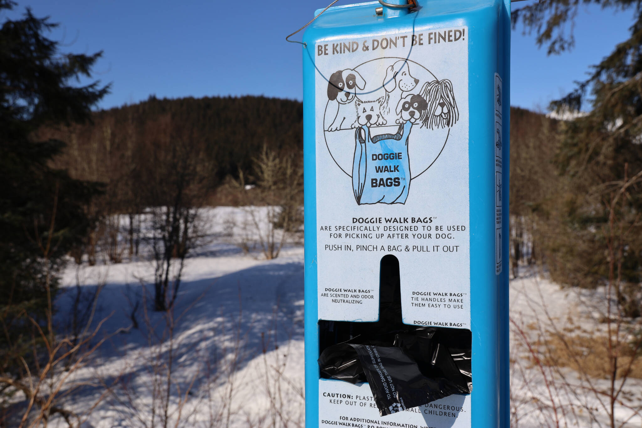 A dog poop bag dispenser sits filled with bags ready for use at the entrance of Kaxdigoowu Héen Dei, also known as Brotherhood Bridge Trail. The City and Borough of Juneau spends about $10,000 a year on dog poop bags, officials say, but the issue of owners not picking after their pets persists. (Clarise Larson / Juneau Empire)