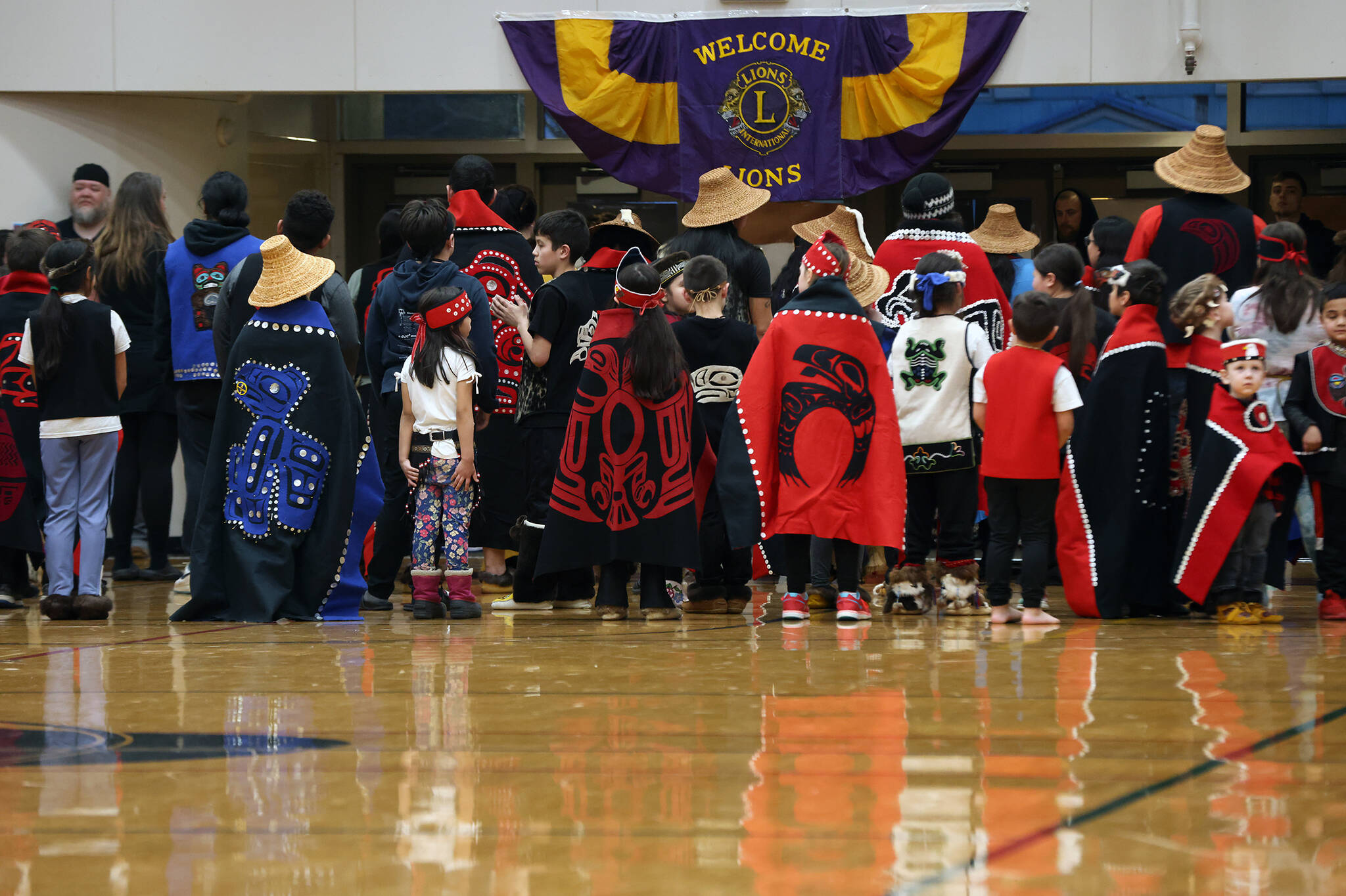 Dancers, including the Eagle Raven Dancers, Wooshji.een and students in the TCLL Program, stand in between songs Thursday evening during a performance ahead of a Gold Medal Basketball Tournament game between Juneau and Hydaburg. (Ben Hohenstatt / Juneau Empire)
