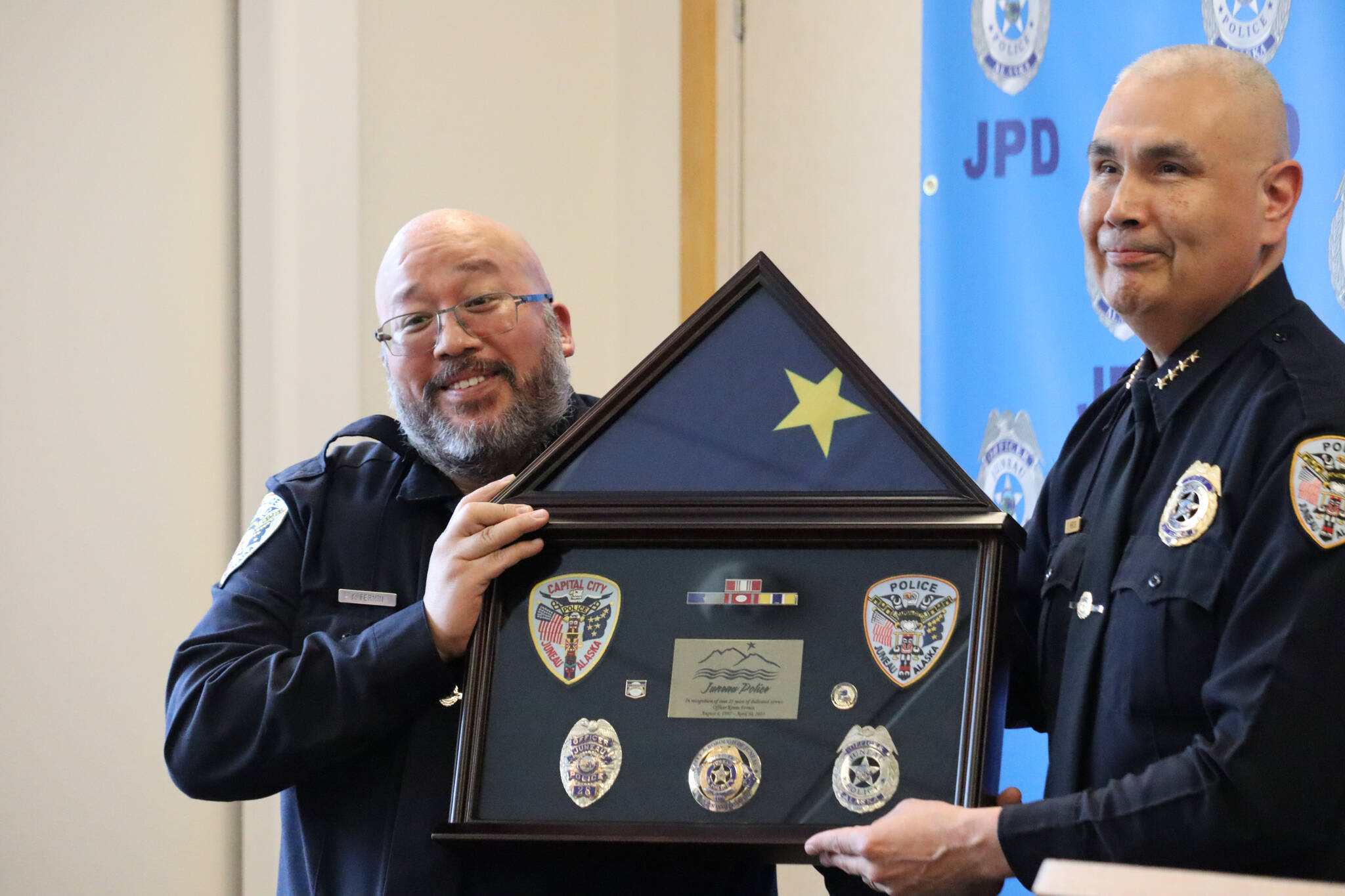JPD Officer Kevin Fermin stands with Chief Ed Mercer while being presented with Fermin’s shadowbox, which is given to every officer at their retirement ceremony. (Jonson Kuhn / Juneau Empire)