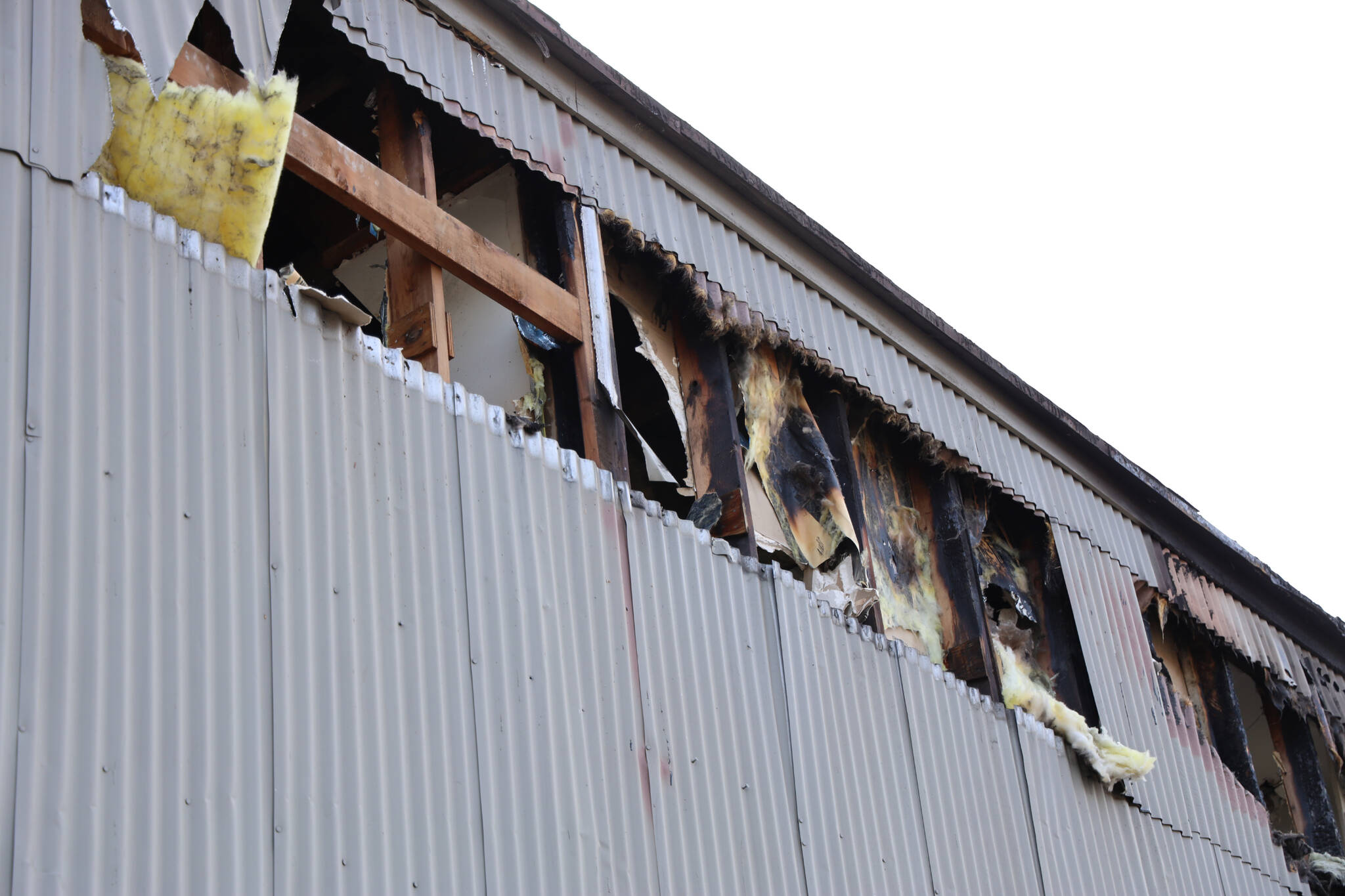 Burnt pieces of insulation can be seen falling from a privately owned airport hangar at the Juneau International Airport after Capital City Fire/Rescue extinguished a fire in the building Thursday morning. (Clarise Larson / Juneau Empire)