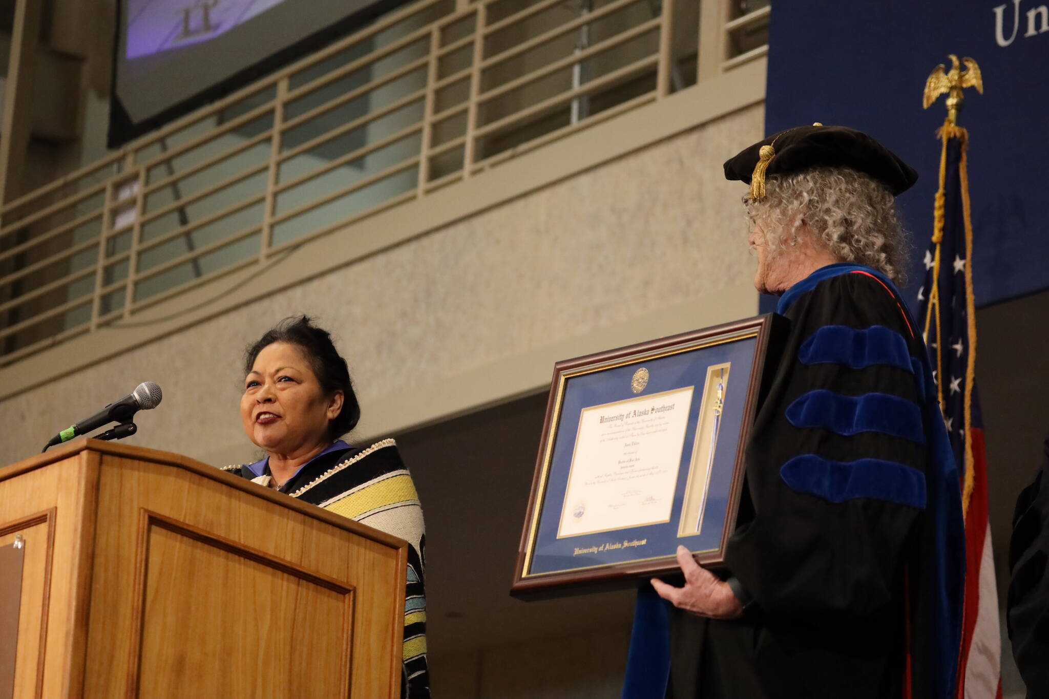 Chilkat weaver Anna Brown Ehlers (left) gives a speech at the 2023 University of Alaska Southeast commencement ceremony Sunday afternoon as Chancellor Karen Karey (right) holds Ehler’s honorary Doctorate of Fine Arts she was bestowed during the event. (Clarise Larson / Juneau Empire)