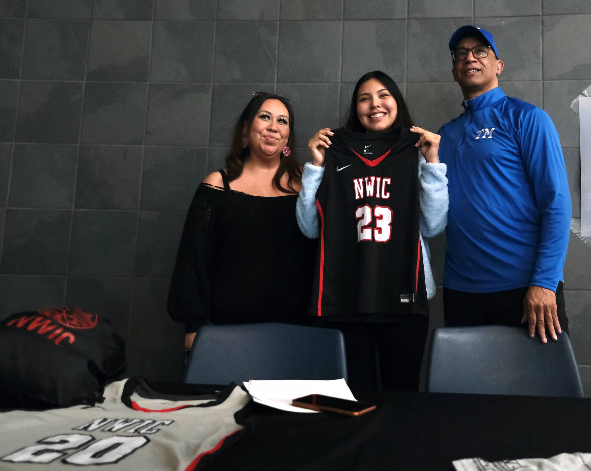 Thunder Mountain High School senior Kiara Kookesh holds a Northwest Indian College jersey after signing to play college basketball for the Bellingham, Washington, school on Monday while flanked by her mother Marcie Kookeshand TMHS coach Andy Lee. (Klas Stolpe / Juneau Empire)