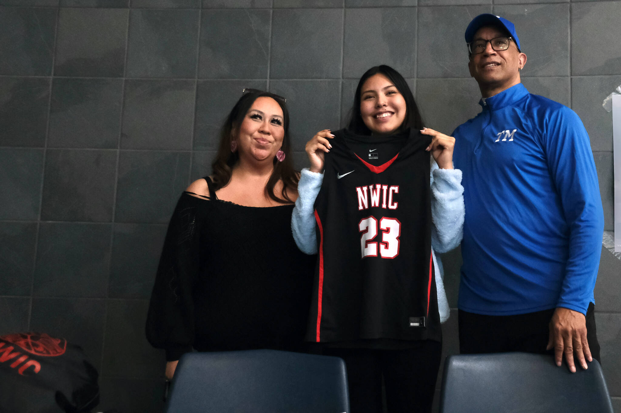 Thunder Mountain High School senior Kiara Kookesh holds a Northwest Indian College jersey after signing to play college basketball for the Bellingham, Washington, school on Monday while flanked by her mother Marcie Kookesh and TMHS coach Andy Lee. (Klas Stolpe / Juneau Empire)