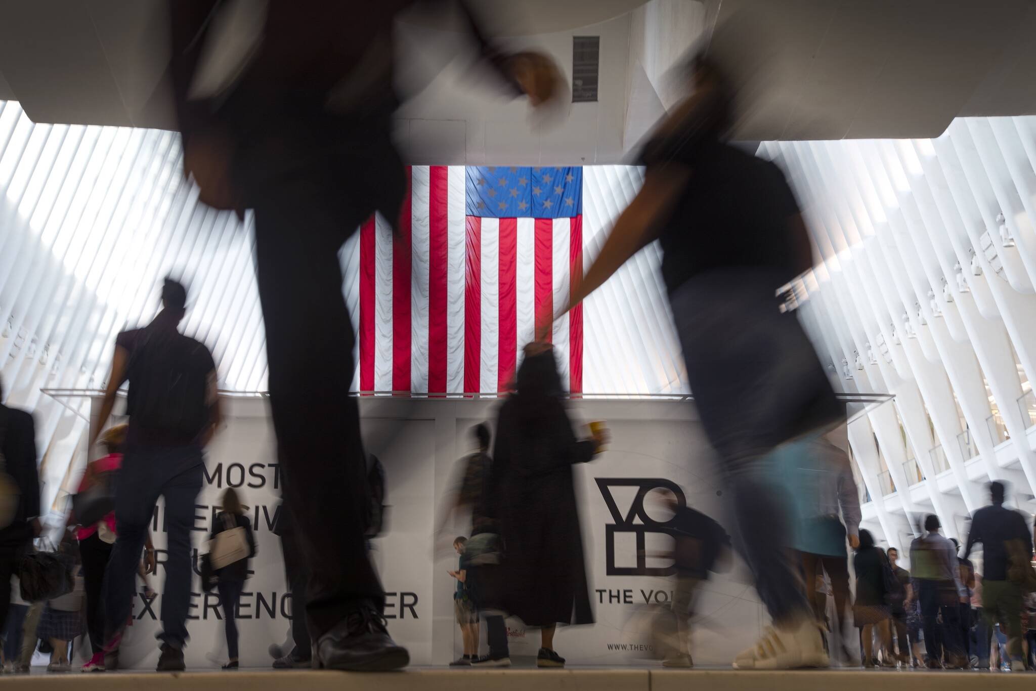 People walk past an American flag inside the Oculus, part of the World Trade Center transportation hub, at the start of a work day in New York, Sept. 11, 2019. American lore is full of tales of a nation built on the foundations of individualism. In reality, loneliness in America can be deadly. In May 2023, the U.S. surgeon general declared it an epidemic, saying that it takes as deadly a toll as smoking. (AP Photo / Wong Maye-E)