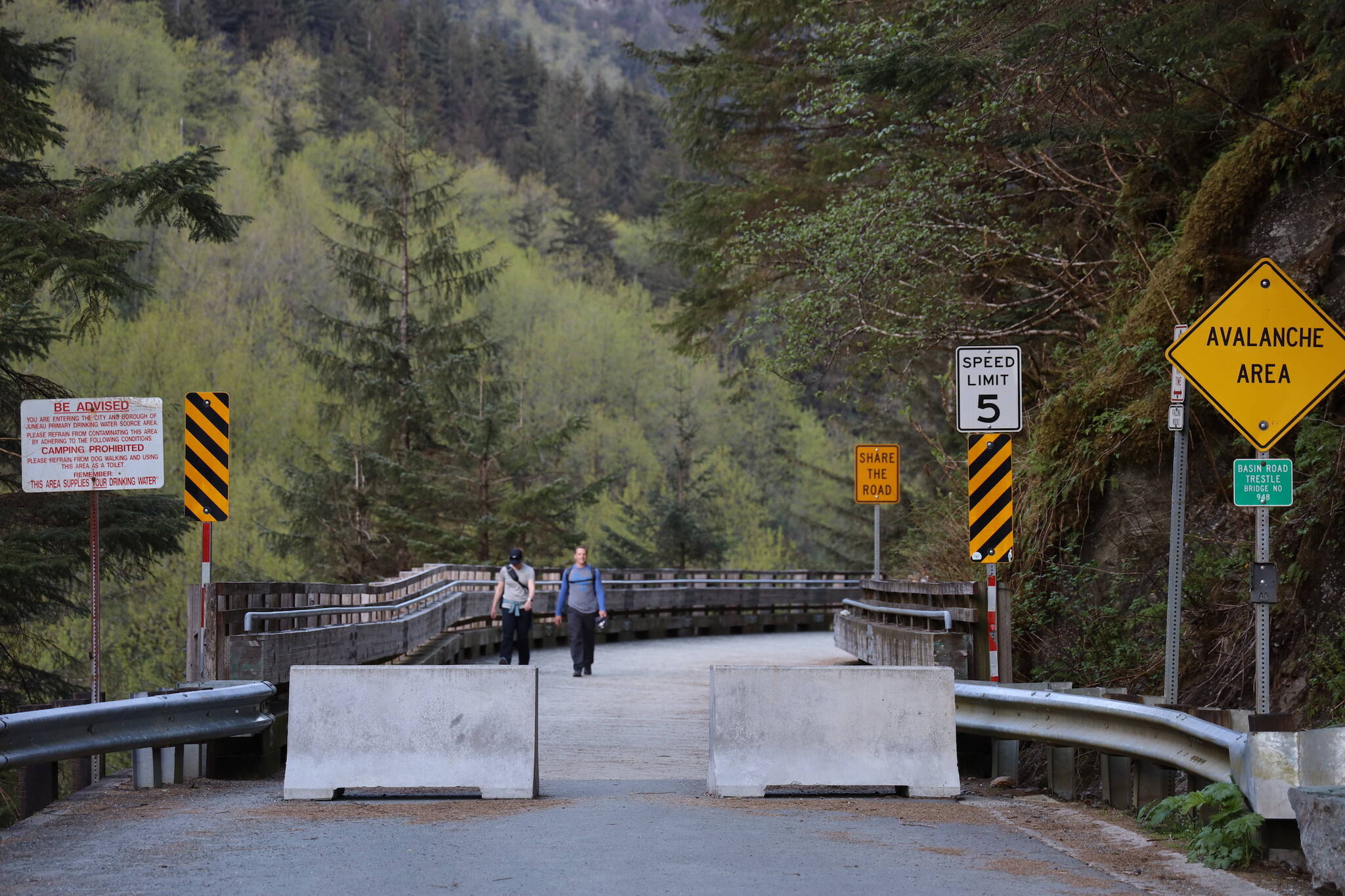 People walk along the Basin Road Trestle Tuesday evening as concrete barricades block off its entrance. The trestle is set to close to pedestrian traffic spanning from May 26 to June 11 between 7 a.m. and 7 p.m. while a contracted construction company repairs damages the trestle suffered in January from a rockslide. (Clarise Larson / Juneau Empire)