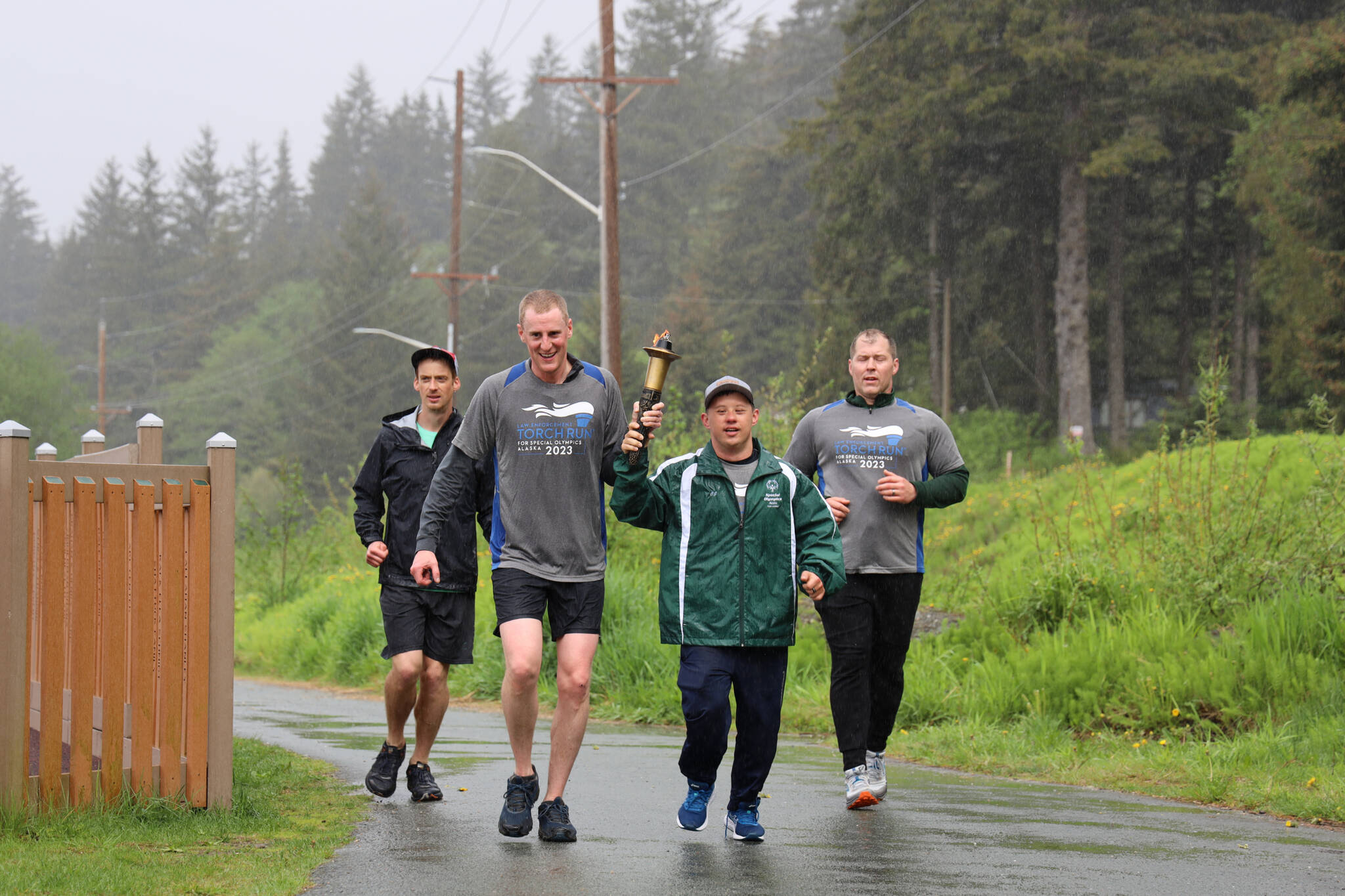 Branden Forst (left center) carries the torch with C.J. Umbs (right center) before crossing the finish line during the Alaska Law Enforcement Torch Run at Twin Lakes Park Saturday morning. (Clarise Larson / Juneau Empire)