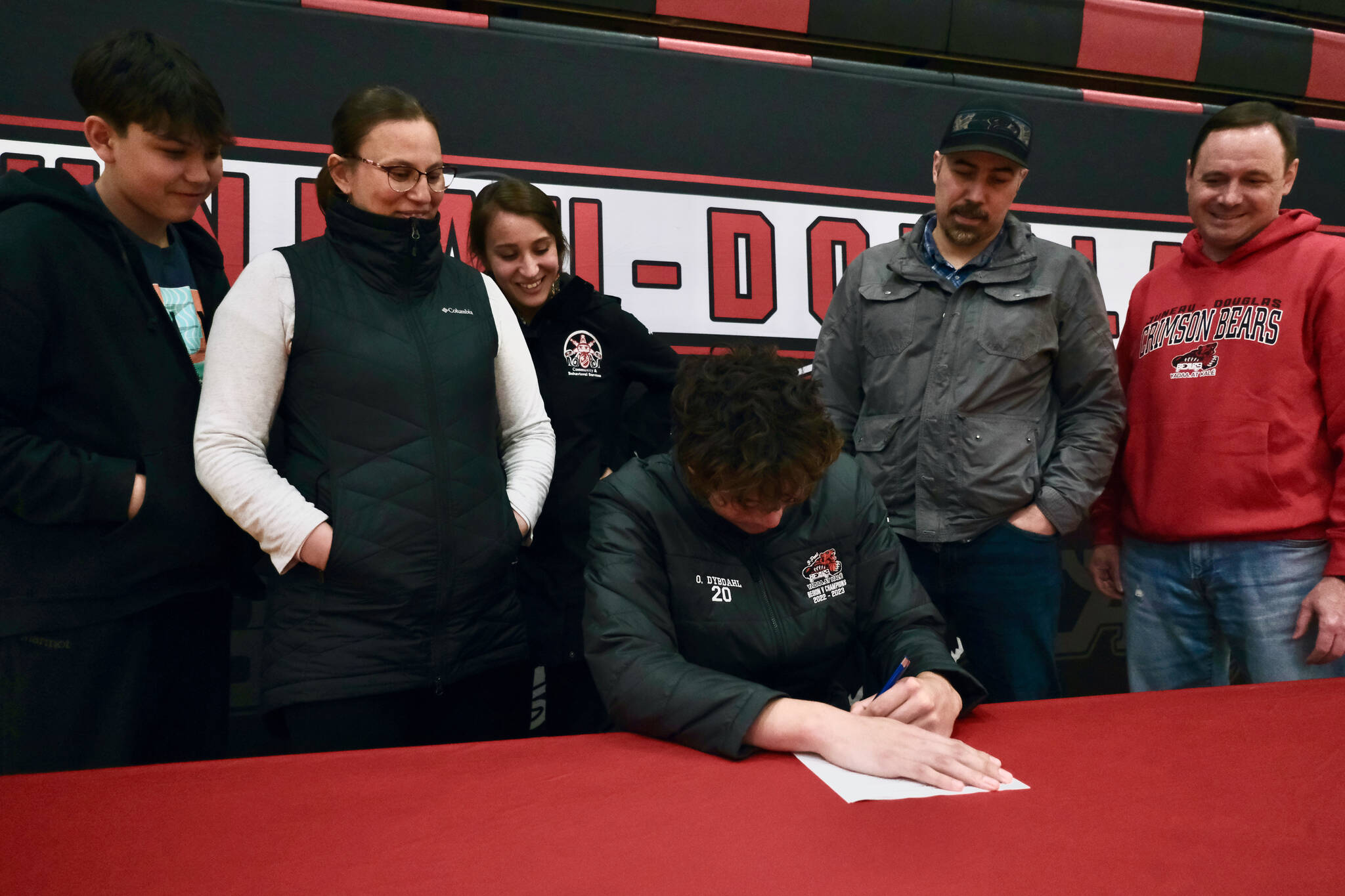 Juneau-Douglas High School: Yadaa.at Kalé Crimson Bears center Orion Dybdahl signs a letter of intent Monday to play basketball at Centralia College as brother Eli Dybdahl, mother Sarah Dybdahl, sister Michaela Demmert, father Travis Dybdahl and JDHS coach Robert Casperson look on Monday at the JDHS gym. (Klas Stolpe / Juneau Empire)