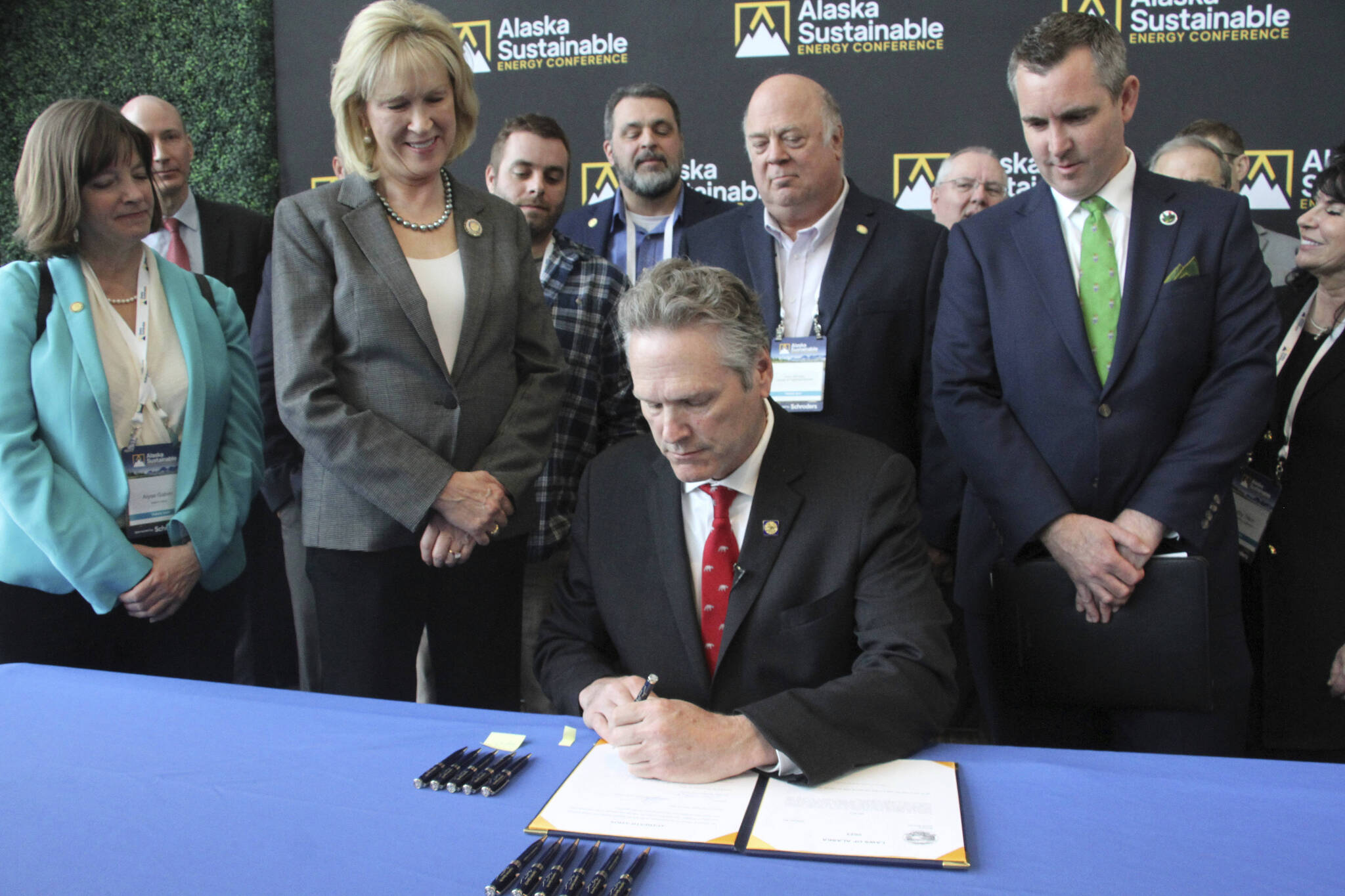 Gov. Mike Dunleavy signs legislation allowing the state to set up a carbon offset program Tuesday in Anchorage. Dunleavy signed the bill with Alaska lawmakers and administration officials standing behind him during the Alaska Sustainable Energy Conference at the Dena’ina Civic and Convention Center in downtown Anchorage. (AP Photo/Mark Thiessen)