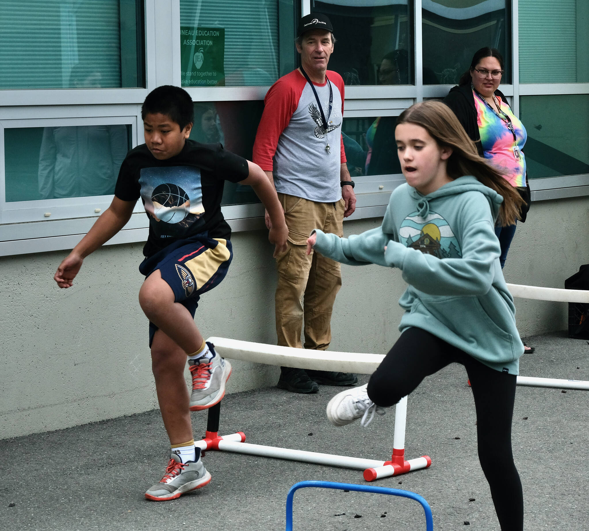 Sayéik: Gastineau Community School physical education teacher Dirk Miller watchs students William Olmstead and Allie Simonson clear hurdles during Field Day at the school on Thursday. Miller is retiring after 24 years at the school. (Klas Stolpe / Juneau Empire)