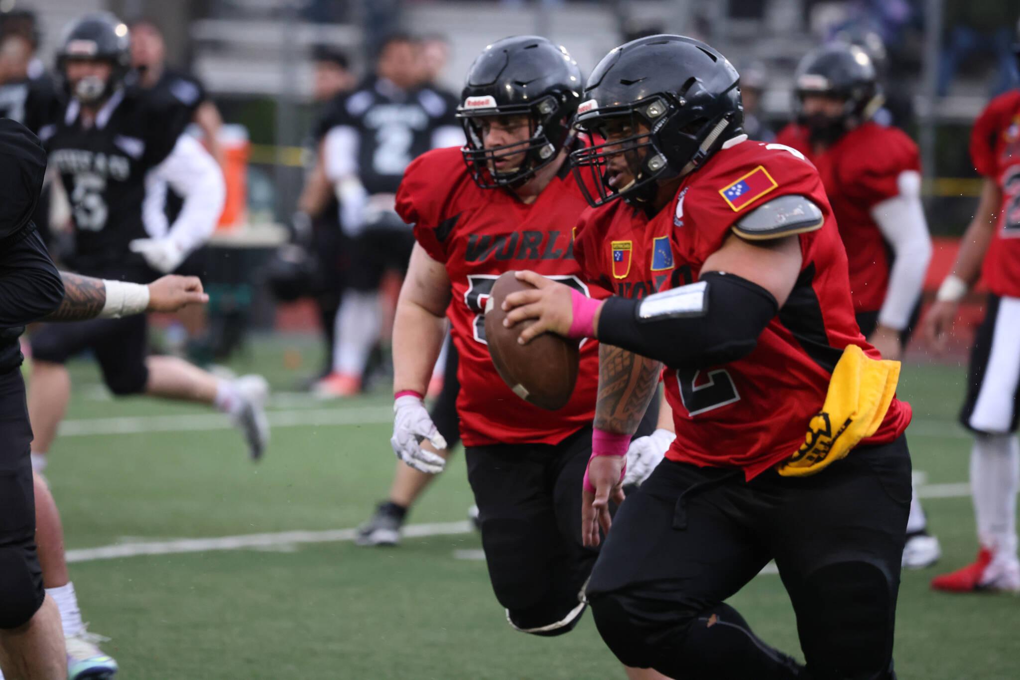 Team World’s Lance Fenumiai (2), JDHS class of 2018, rushes down the field while teammate Tristan Thomas (50), class of 2015, looks to throw a block during the 2023 Alumni Game played Friday at Adair-Kennedy Field. (Ben Hohenstatt / Juneau Empire)