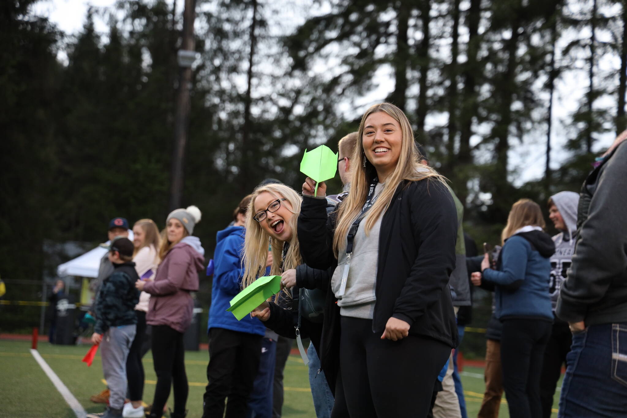 Michaela Meneoza (left) and Anne Coogan (right) smile before launching their paper airplanes during a half-time contest at the Juneau Alumni Football game Friday evening at Adair-Kennedy Field. (Clarise Larson / Juneau Empire)