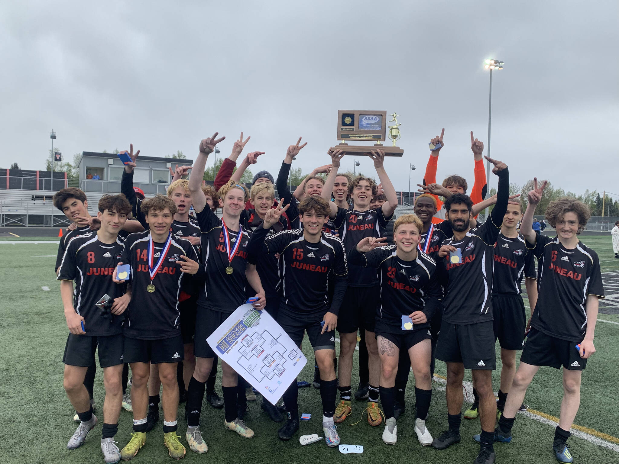 The Juneau-Douglas High School: Yadaa.at Kalé Crimson Bears boys soccer team pose with their championship trophy after defeating Soldotna 4-0 for the ASAA DII Boys Soccer State Championship, Saturday, at West Anchorage High School (Courtesy Photo / JDHS Soccer)