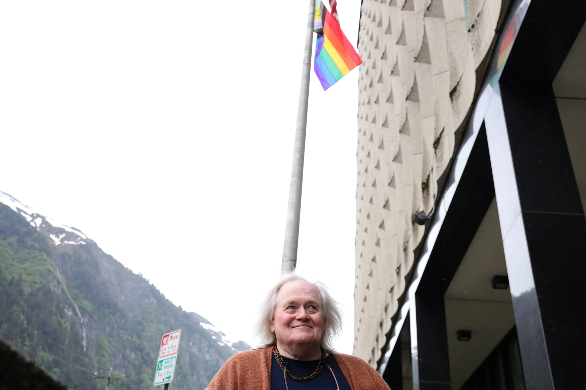 Writer Jane Hale smiles for a photo as the wind blows a newly raised LGBTQ+ flag at the Hurff A. Saunders Federal Building downtown. (Clarise Larson / Juneau Empire)