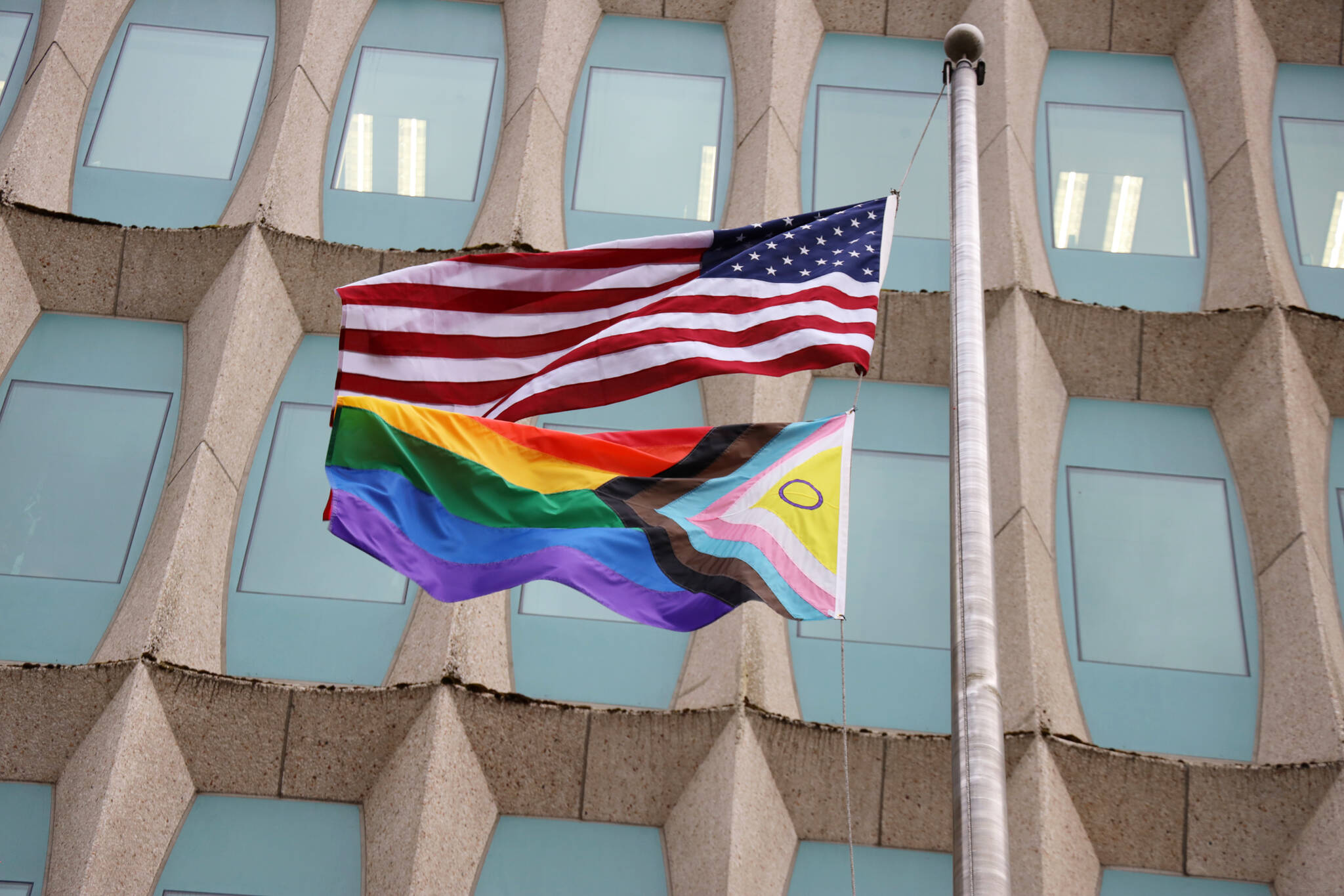 A progress pride flag flies in the wind below an U.S. flag outside of the Hurff Ackerman Saunders Federal Building on Monday evening. Last week the flag was raised for the first time by members of the National Oceanic Atmospheric Administration and will remain up through the month of June. (Clarise Larson / Juneau Empire)