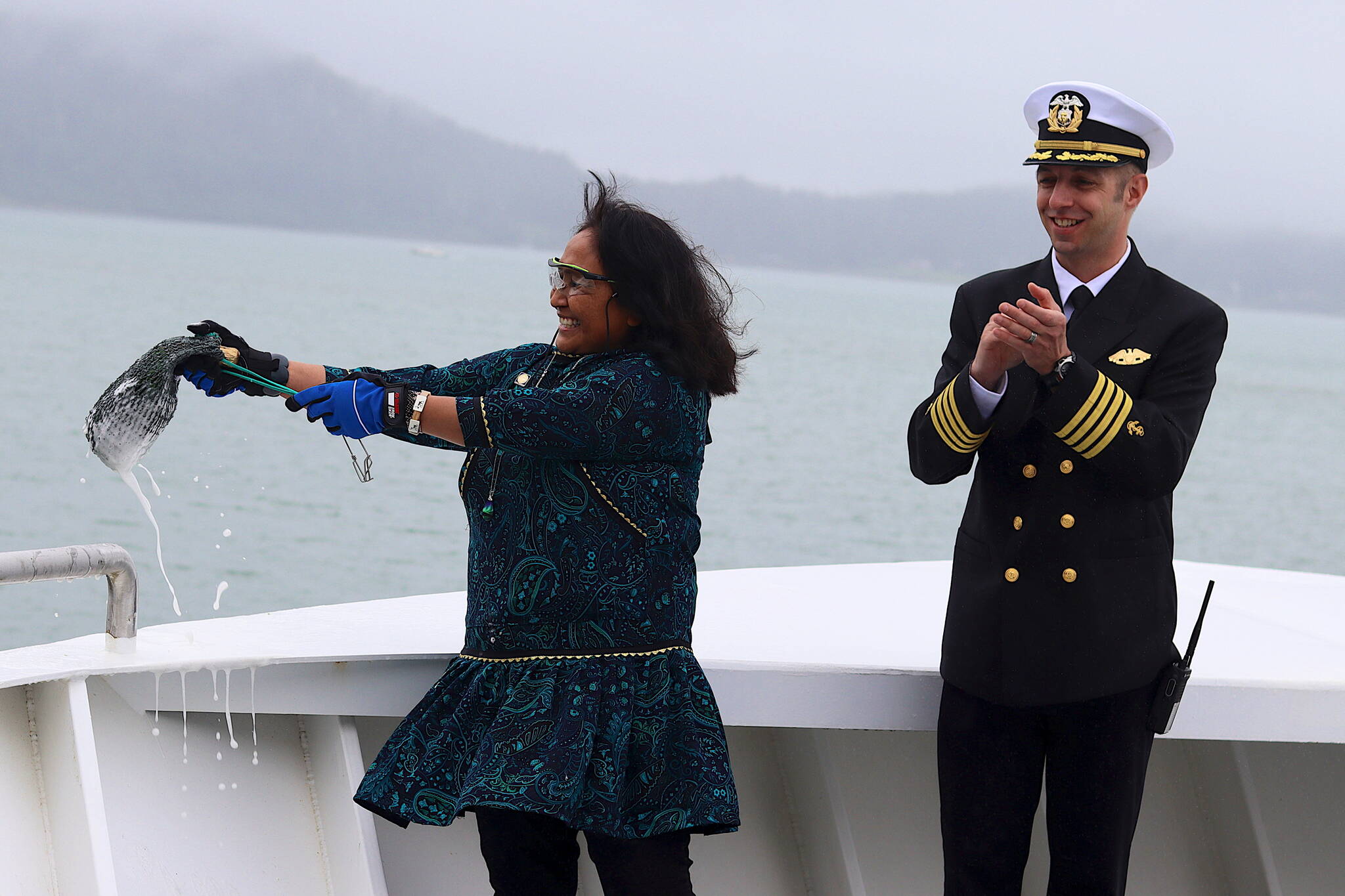 First Lady Rose Dunleavy (left) breaks a bottle across the bow of the Hubbard ferry during a christening ceremony Monday at the Alaska Marine Highway System terminal in Juneau, as vessel relief captain Ethan Waldvogel watches. (Mark Sabbatini / Juneau Empire)
