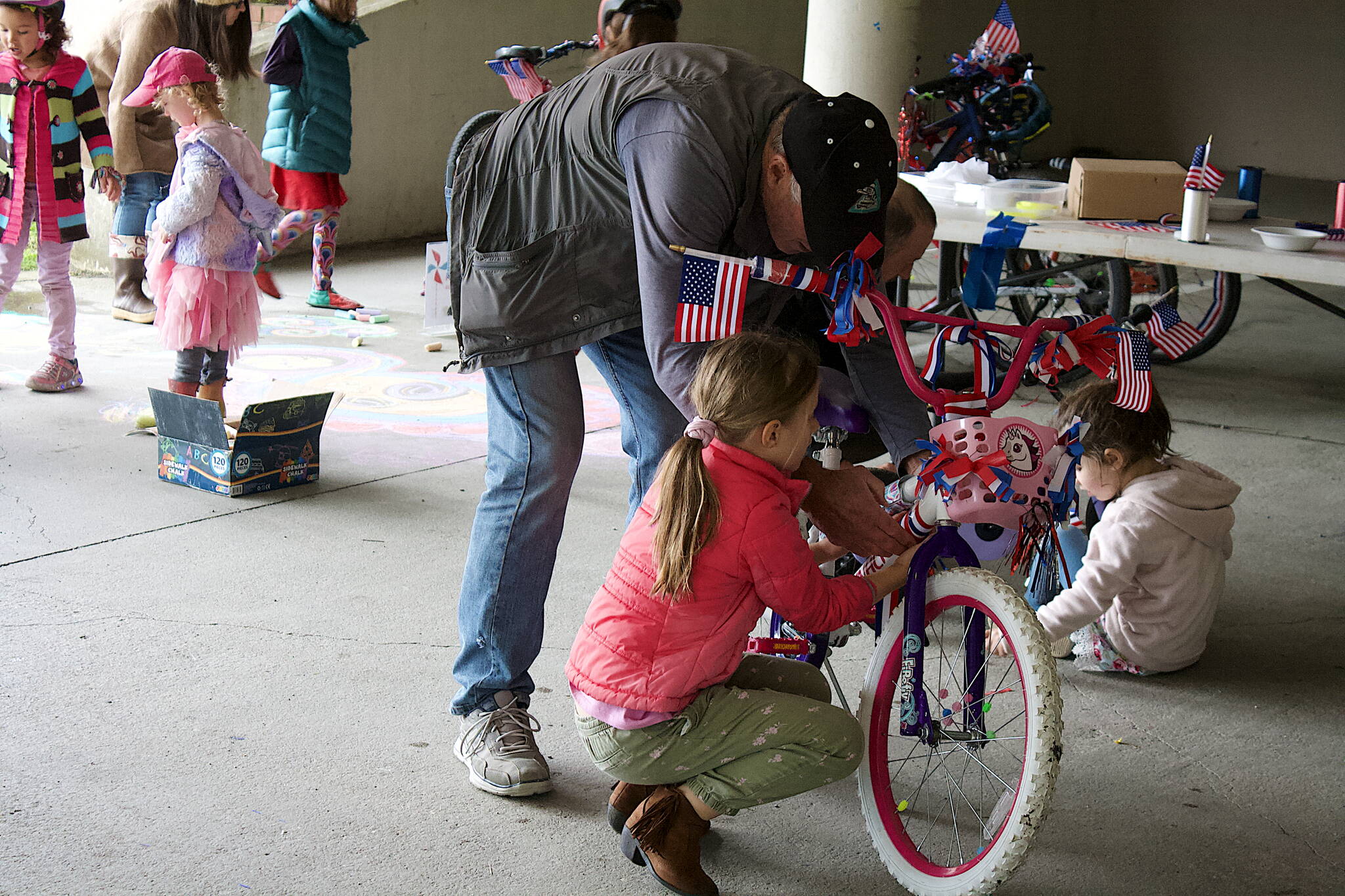 Jim Dalman and his granddaughter Devlin, 6, decorate a bicycle in the Douglas Library parking garage Saturday during the annual pre-July 4 gathering to prepare for the Children’s Parade on Independence Day. (Therese Pokorney / Juneau Empire)