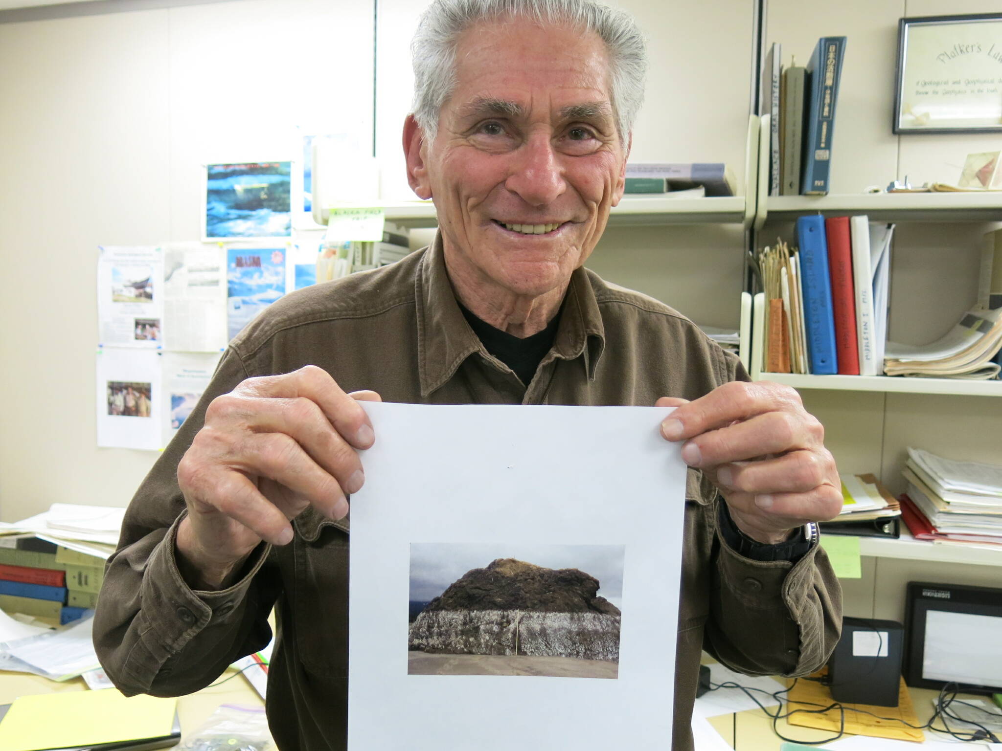 George Plafker holds up a photo of uplifted Alaska shorelines he took after visiting the southern coast following the March 1964 magnitude 9.2 earthquake. Plafker was standing in his office in Menlo Park, California, when this photo was taken in 2013. (Photo by Ned Rozell)