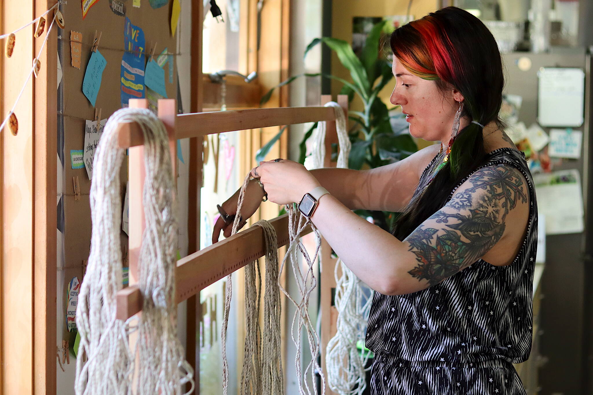 Rae Mills, a mentor with the “Weaving Our Pride” project, hangs strands of wool yarn on a loom that will be used to create two Pride Robes at the Zach Gordon Youth Center on Friday. (Mark Sabbatini / Juneau Empire)