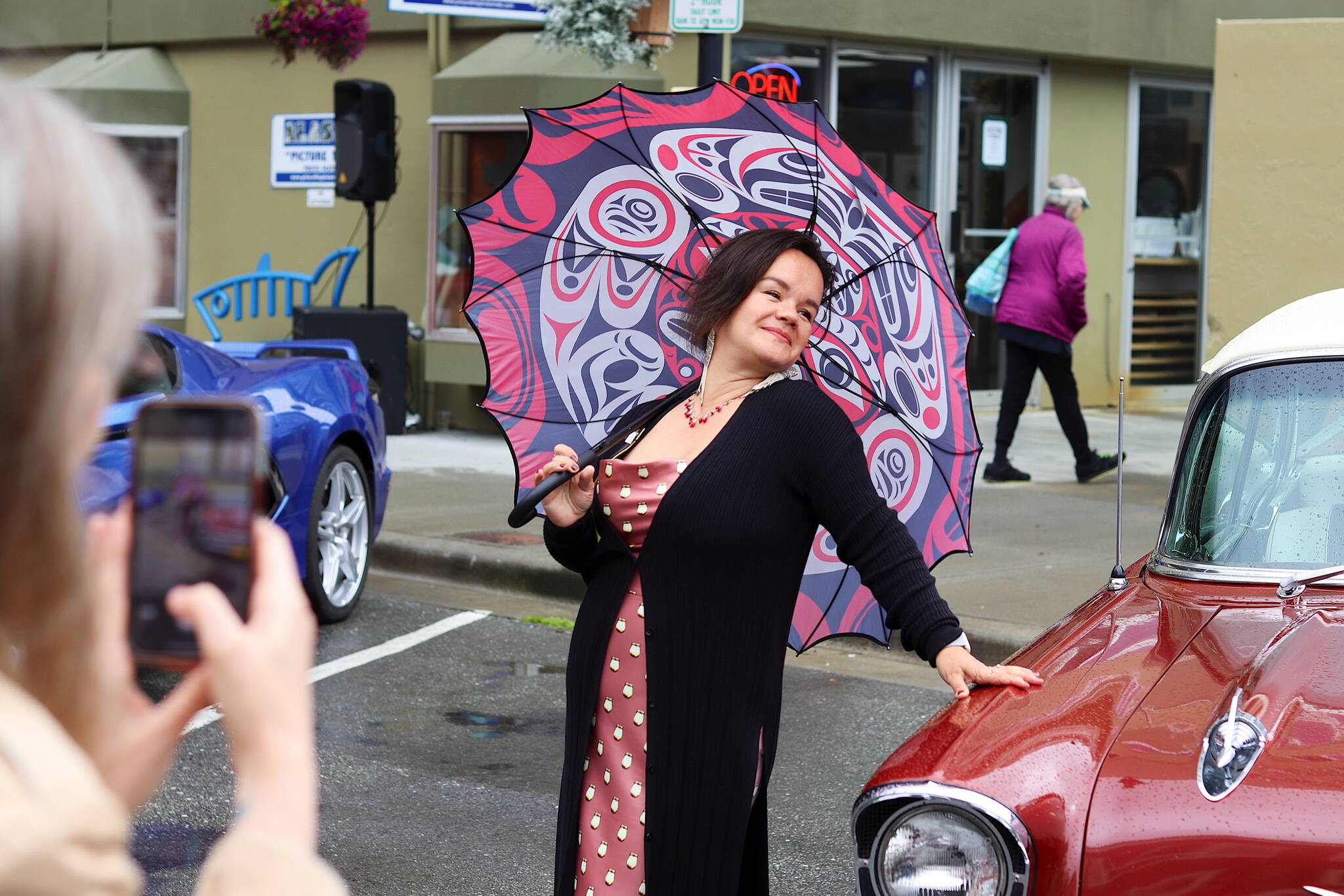 Lily Wooshkindein Da.áat Hope, a Chilkat weaver in Juneau, poses next an antique car for a photo by an audience member during Alaska Fashion Week’s outdoor runway show on Saturday. Hope was among the local designers whose outfits were featured during the show. The antique vehicles were parked along the street to provide ambiance for the outdoor exhibition. (Mark Sabbatini / Juneau Empire)