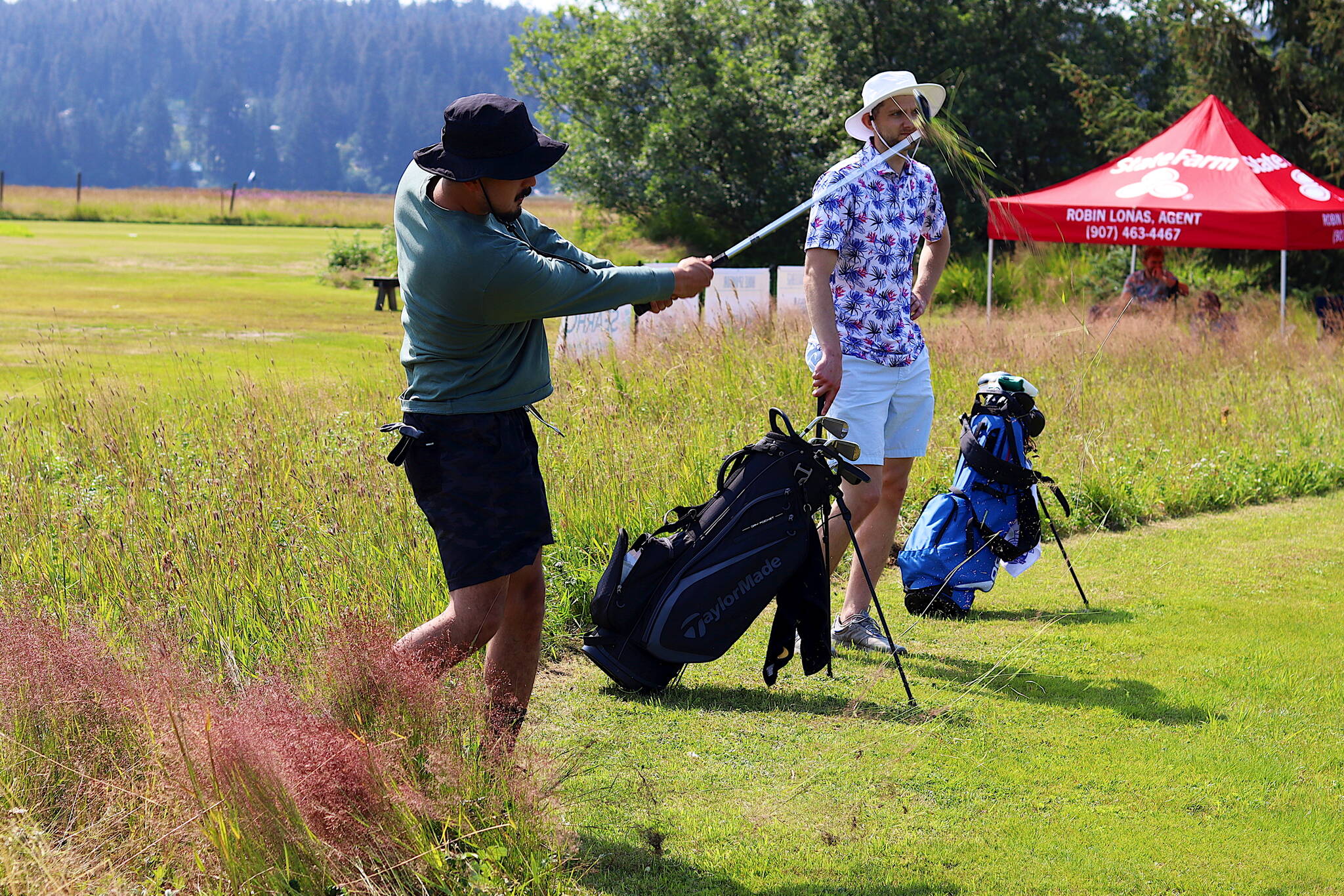 Alan Fisher takes out a big chunk of grass as hits a ball out of the rough as teammate Matt Seymour watches on the seventh hole of the Annual Greater Juneau Chamber of Commerce Golf Classic on Saturday at the Mendenhall Golf Course. (Mark Sabbatini / Juneau Empire)