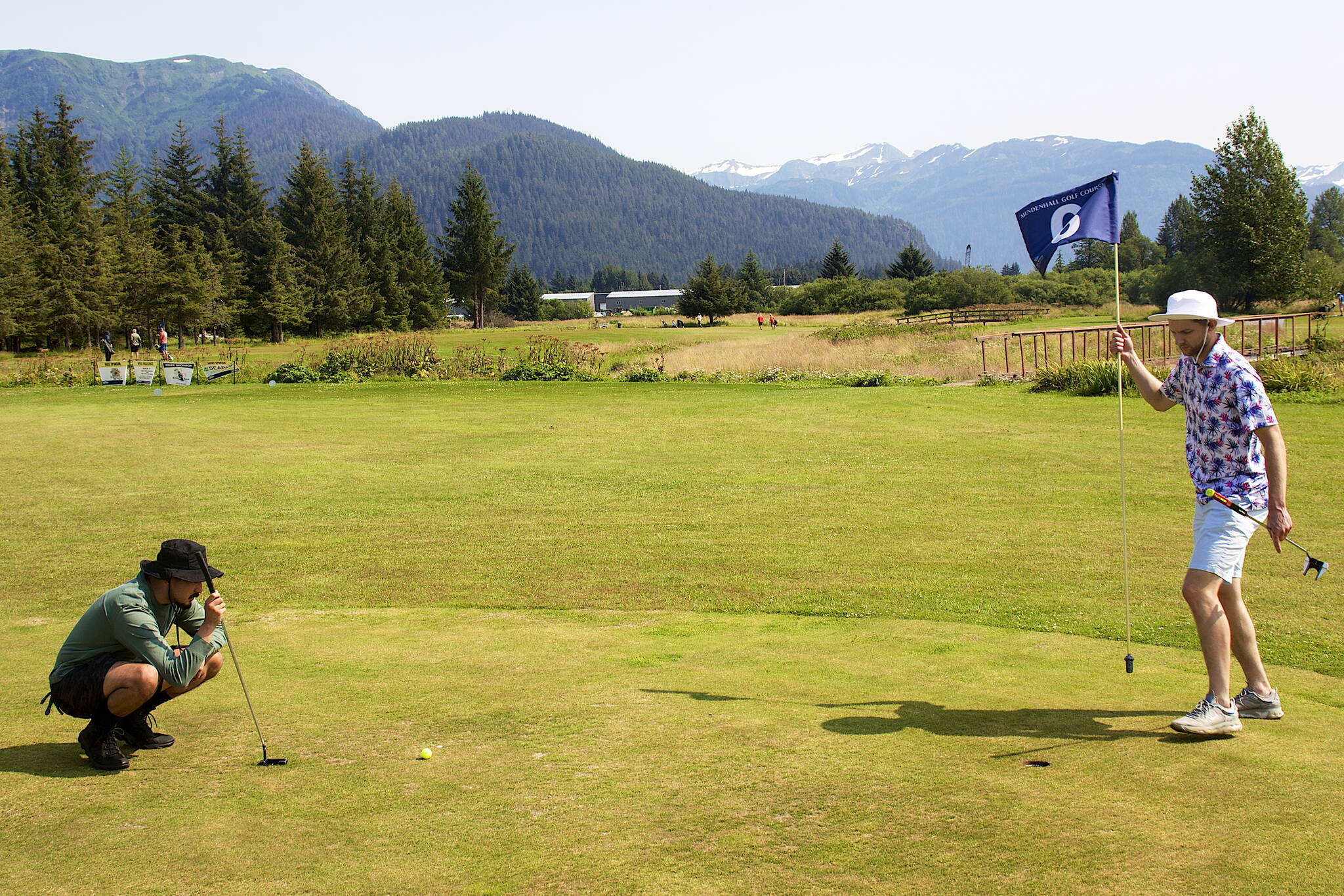Alan Fisher evaluates a putt on the sixth hole as Matt Seymour holds the flag during the Annual Greater Juneau Chamber of Commerce Golf Classic on Saturday at the Mendenhall Golf Course. (Mark Sabbatini / Juneau Empire)